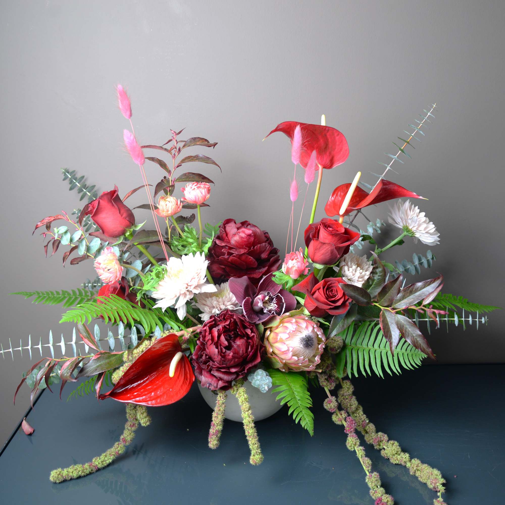 Red and white floral arrangement with anthuriums and roses in a low bowl