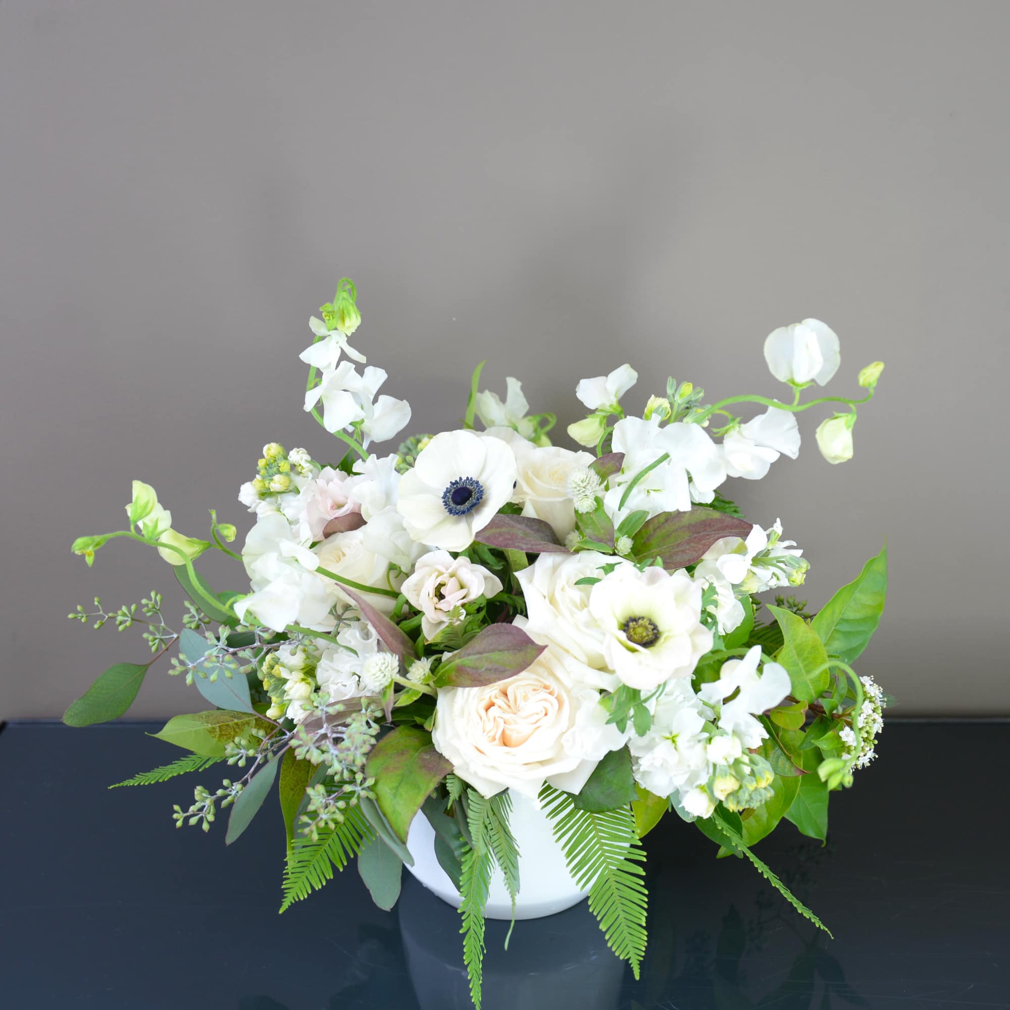 White floral arrangement in a white vase with green foliage
