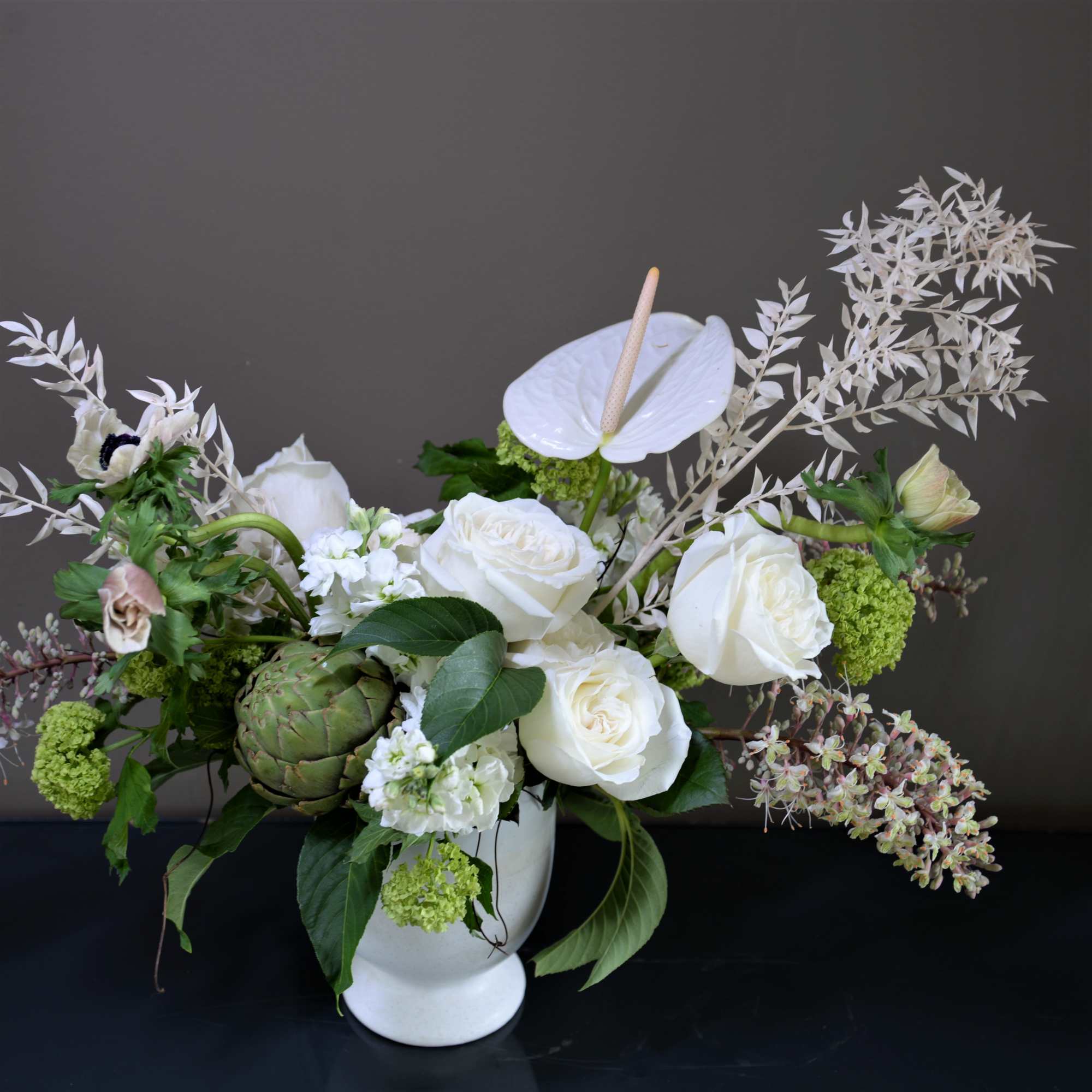 White roses and anthurium in a white vase with green accents