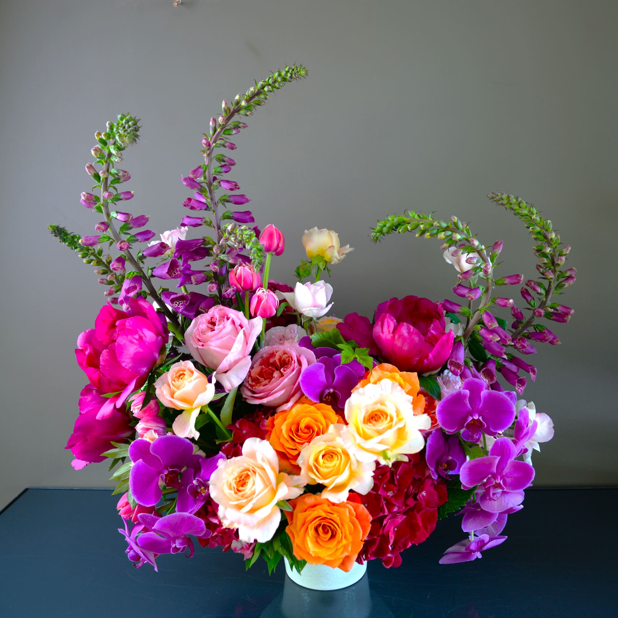 Colorful floral arrangement with roses, peonies, and orchids in a white vase