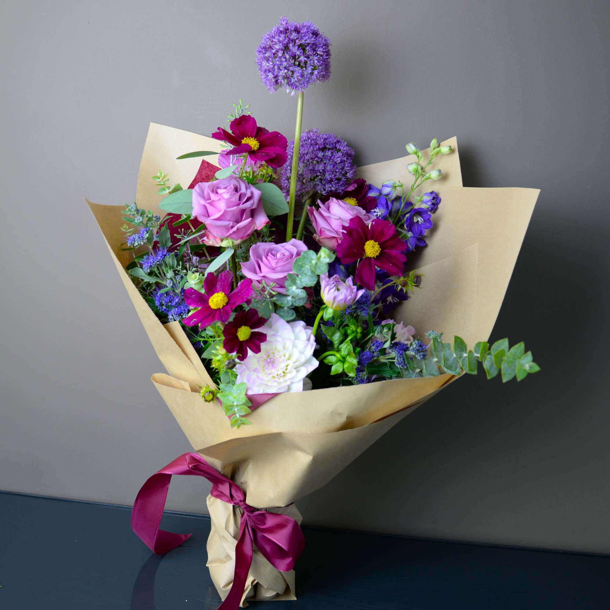 Bouquet of pink roses and purple mixed flowers wrapped in kraft paper