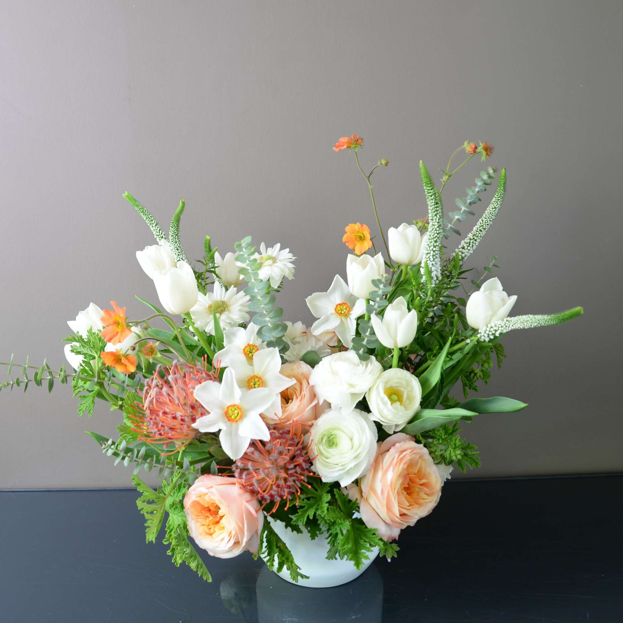 Mixed bouquet of white, peach, and orange flowers in a white vase