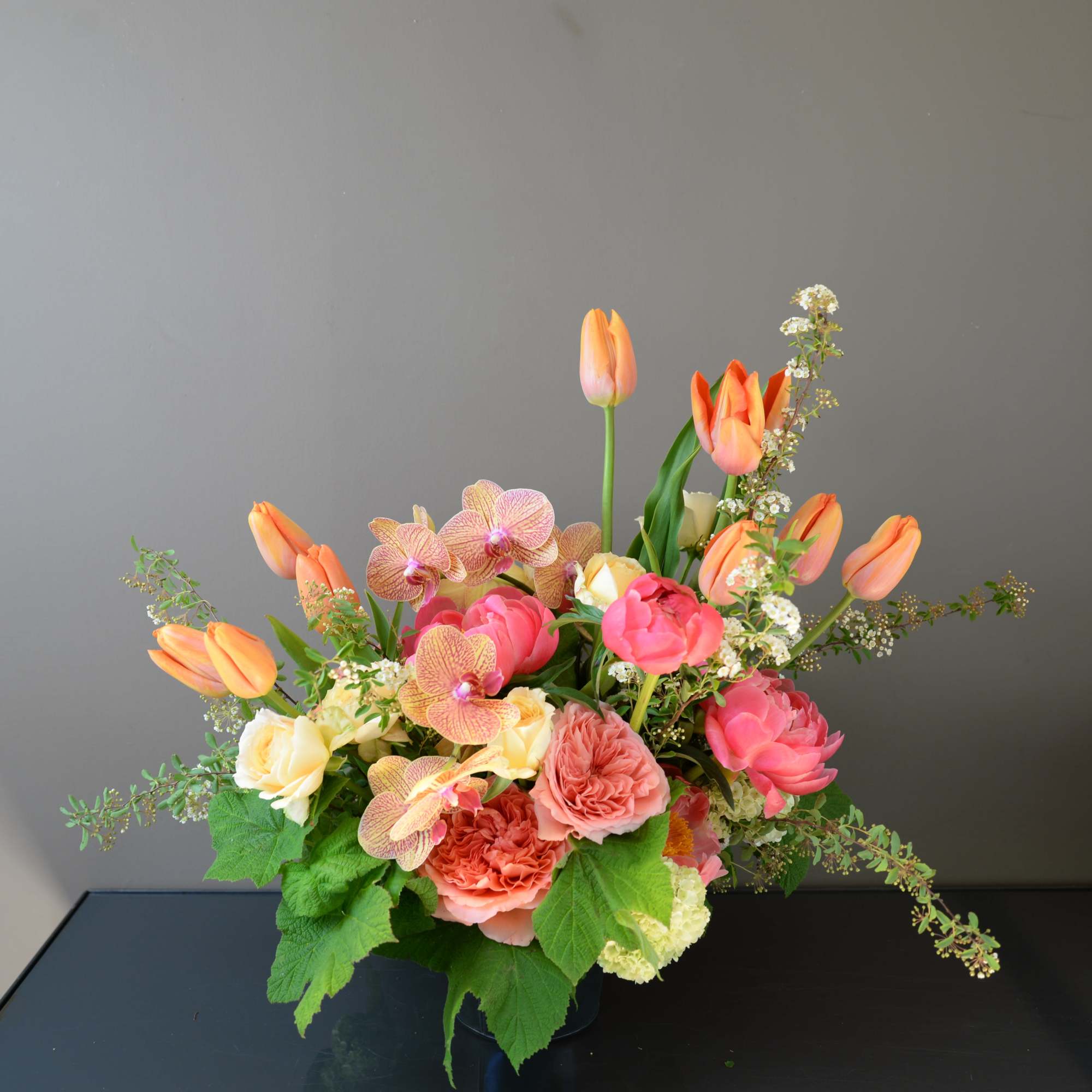 Mixed bouquet of pink and peach flowers in a dark vase