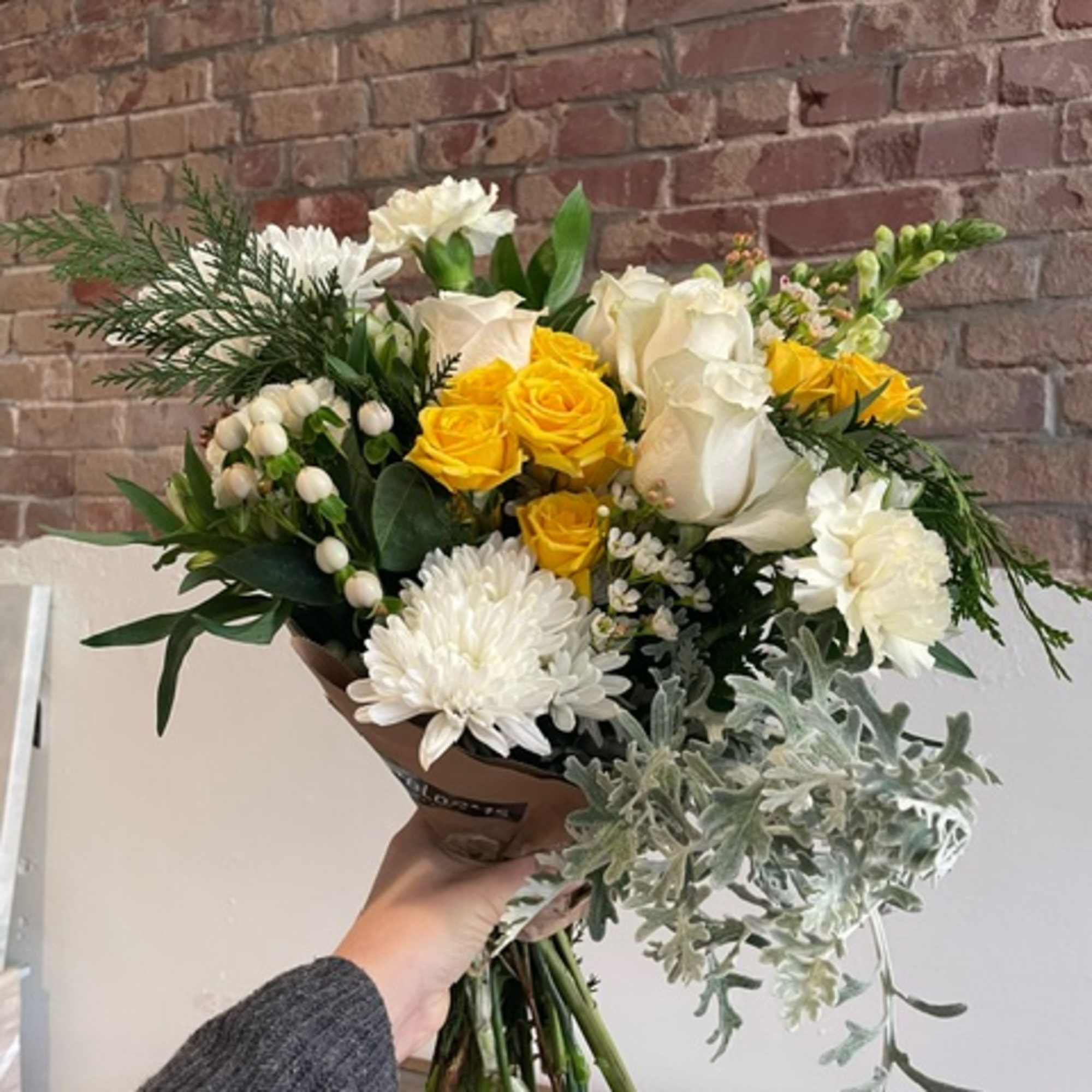 Handheld bouquet of yellow and white roses with white blooms and greenery