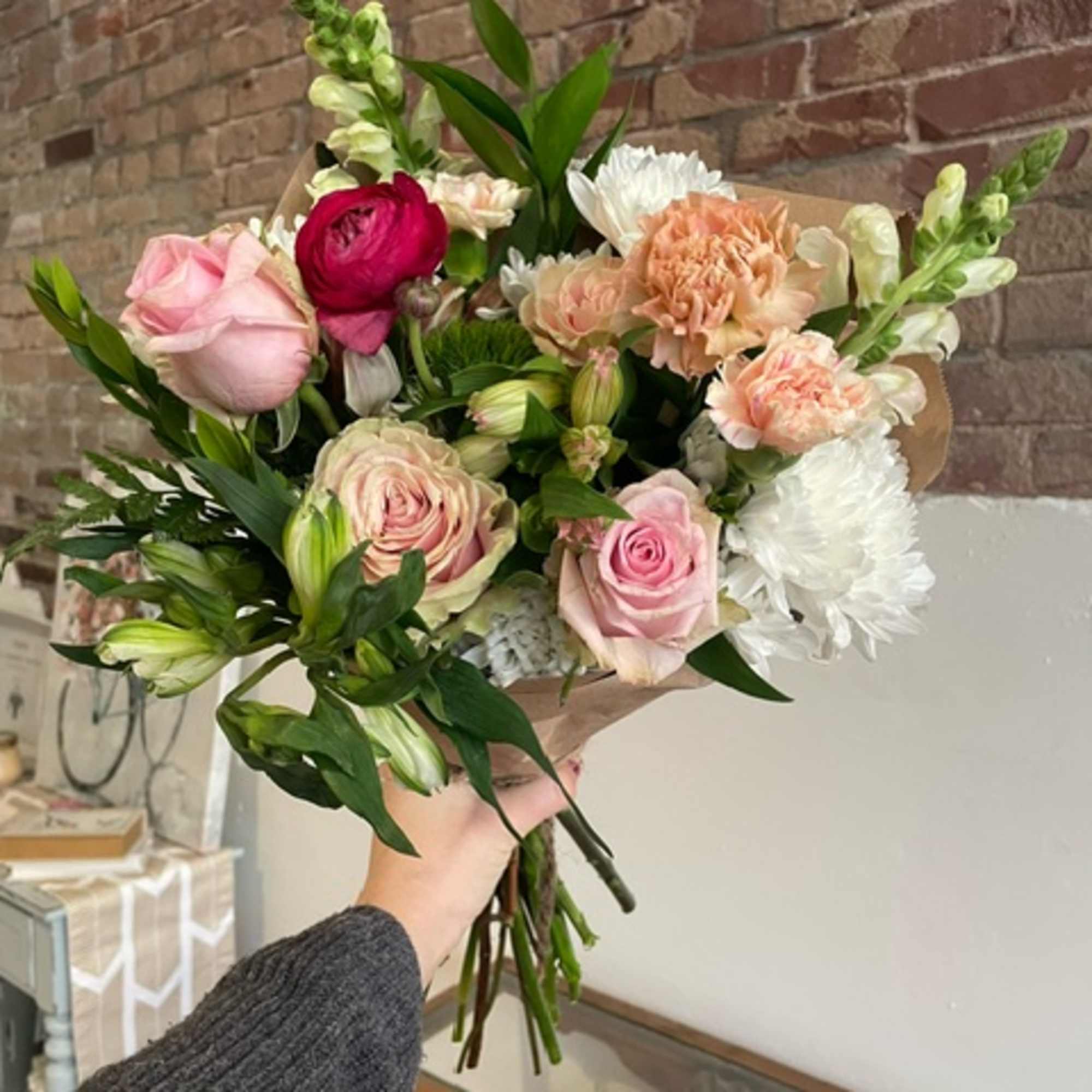 Handheld bouquet of pink and white flowers with greenery