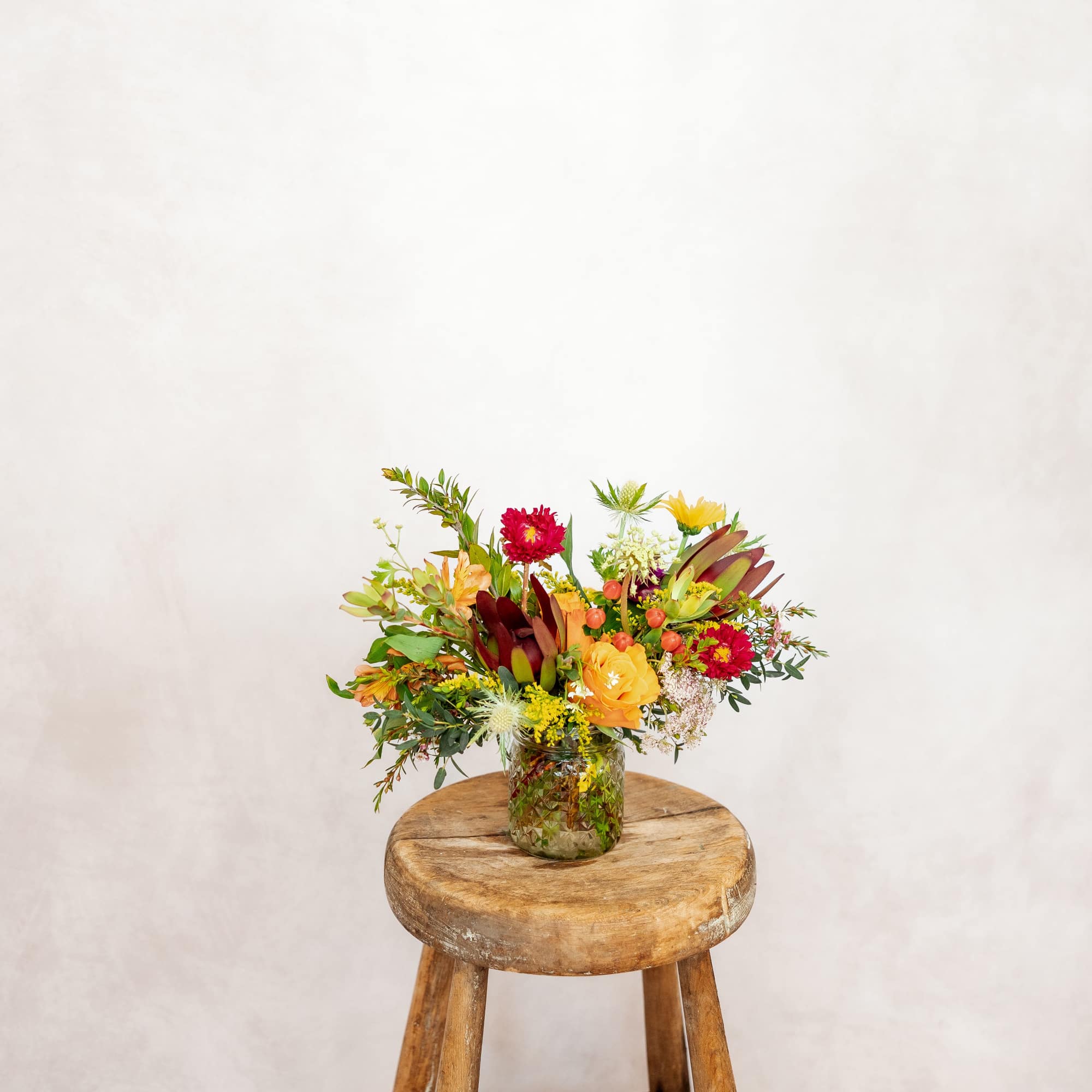 Mixed bouquet in a glass jar on a wooden stool