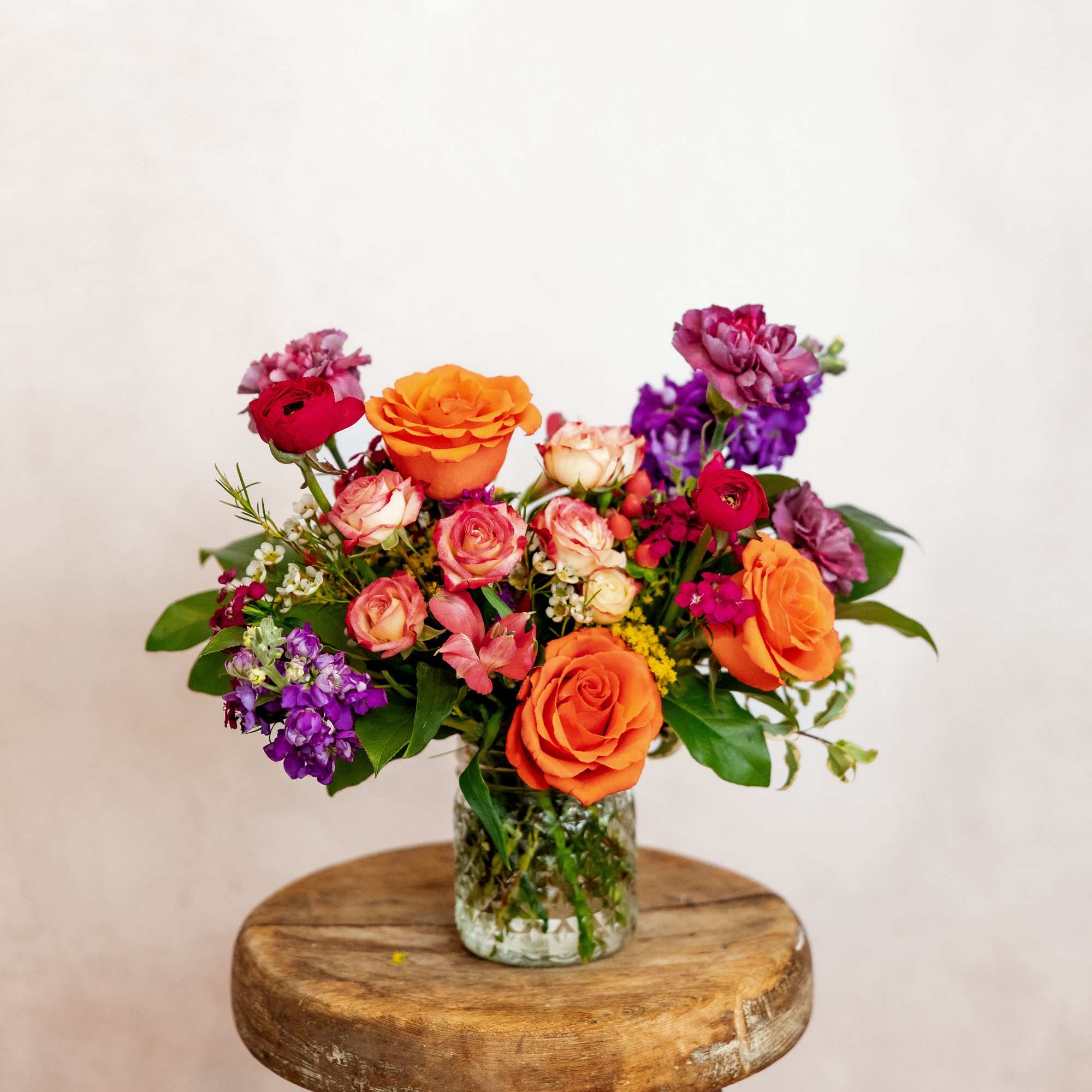 Mixed bouquet of orange, pink, and purple flowers in a glass vase
