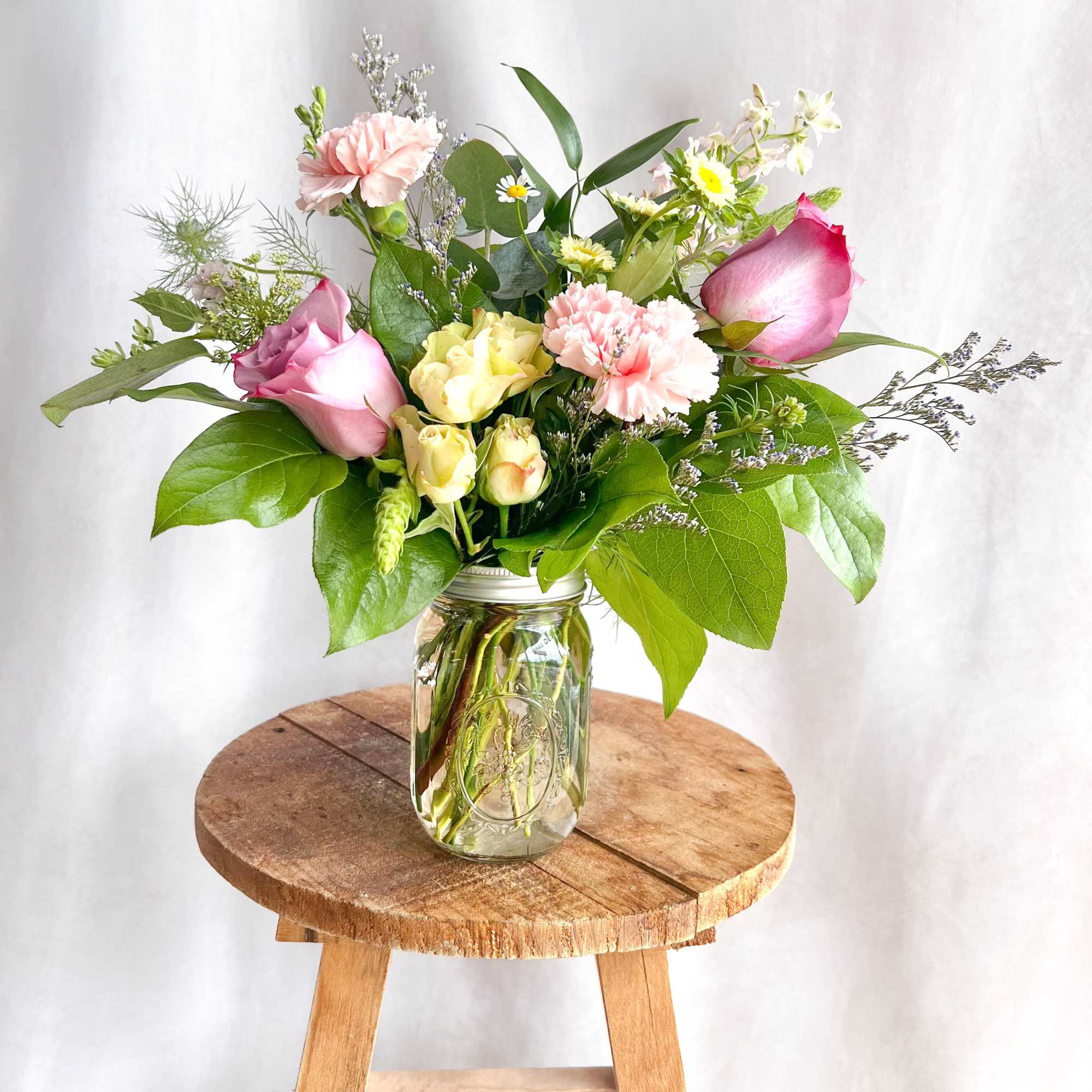 Pink and yellow roses with carnations in a glass jar vase