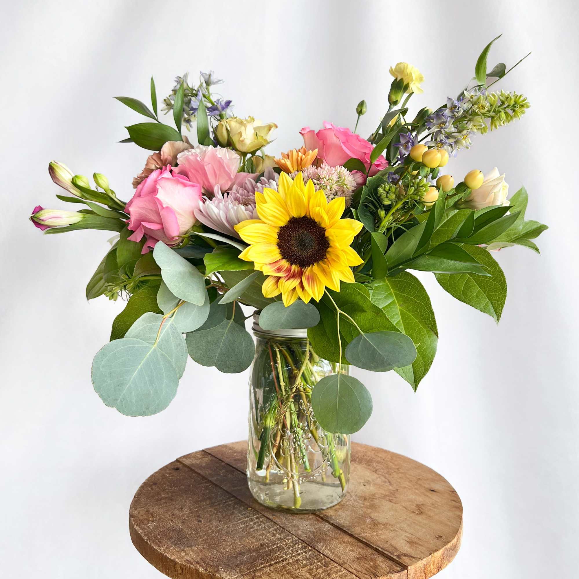 Mixed bouquet with a sunflower, pink roses, and a glass jar vase