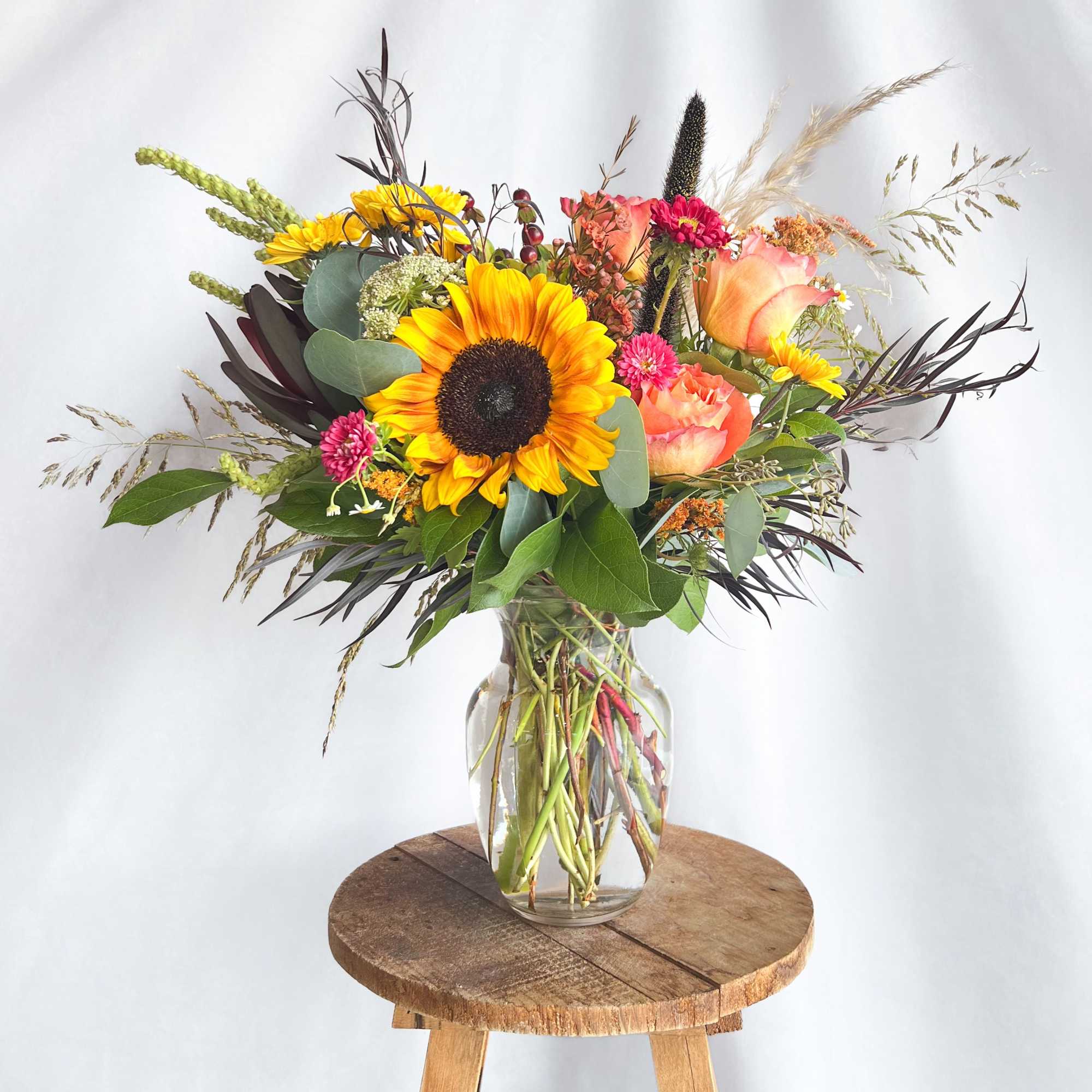 Mixed bouquet with sunflowers, peach roses, and a glass vase