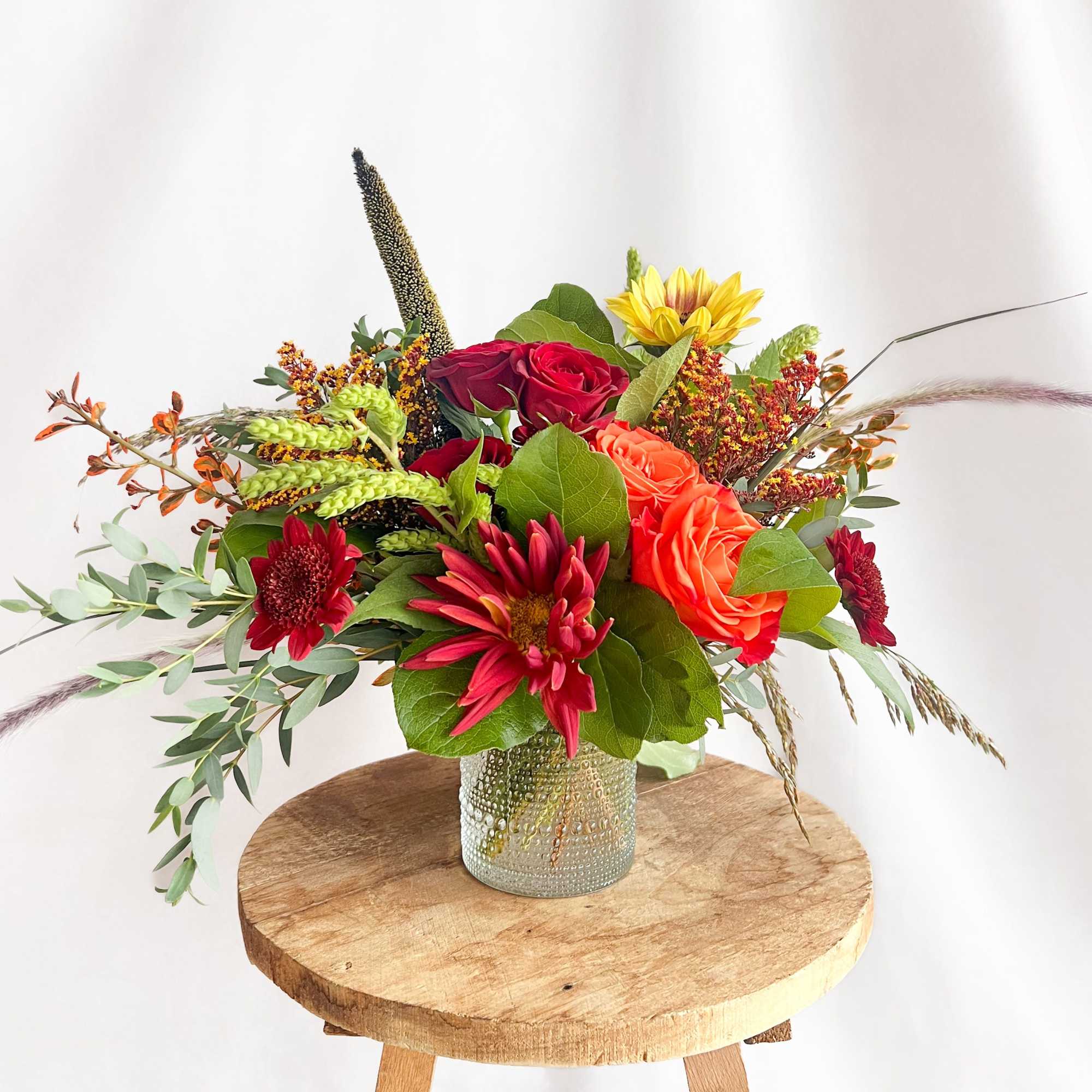 Mixed bouquet of red, orange, and yellow flowers in a textured glass vase