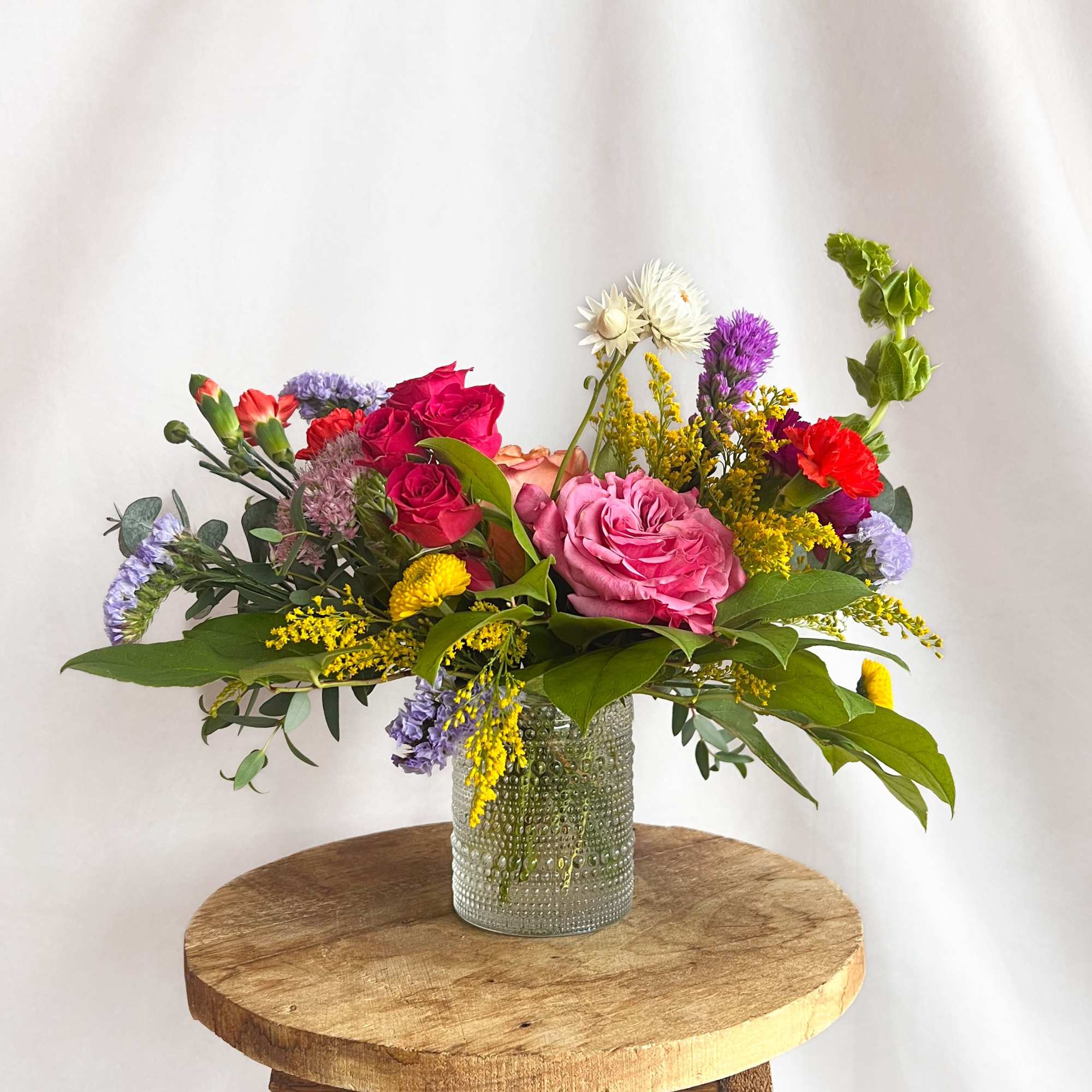 Mixed bouquet in a textured glass vase on a wooden stool