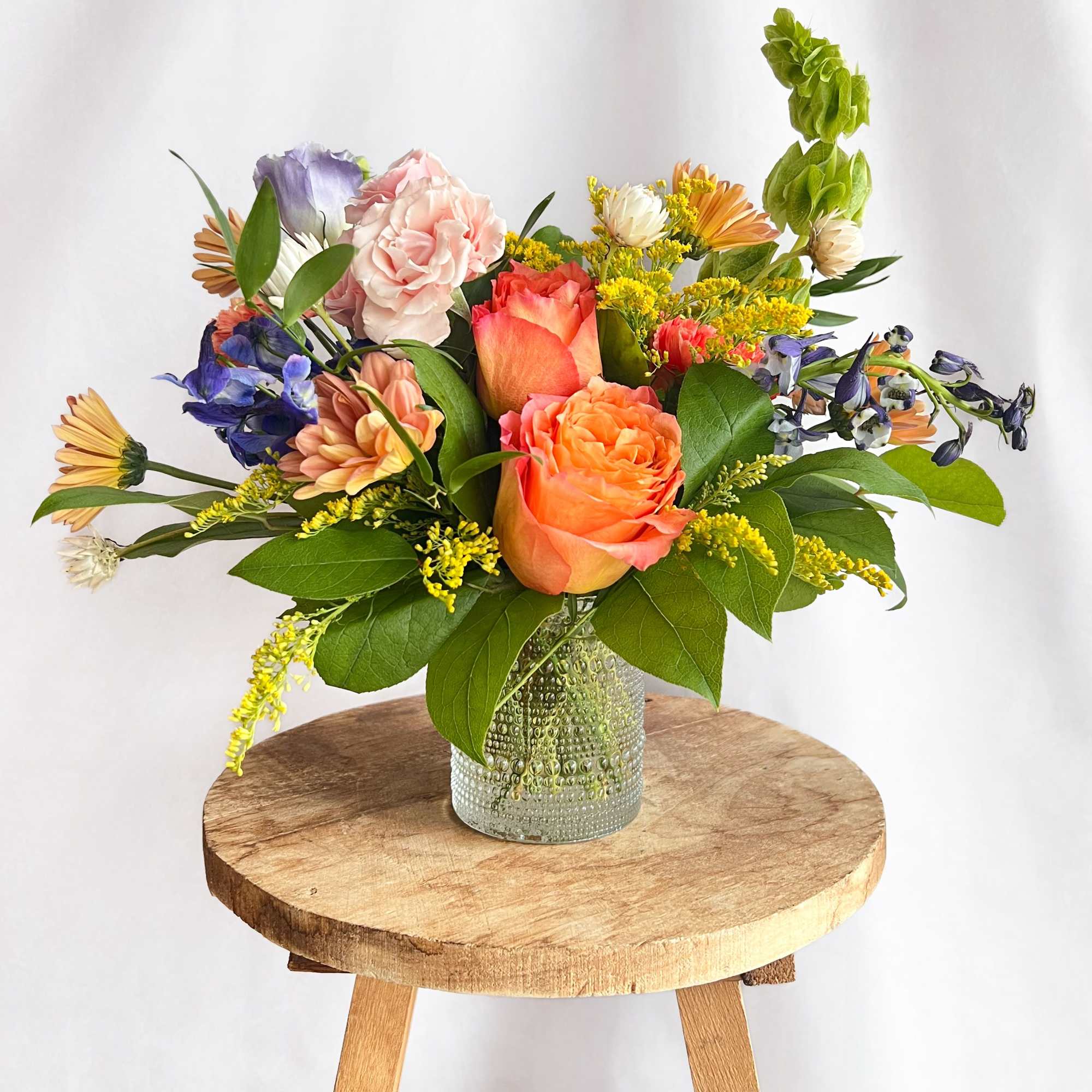 Mixed bouquet in a textured glass vase with peach, pink, purple, and yellow flowers