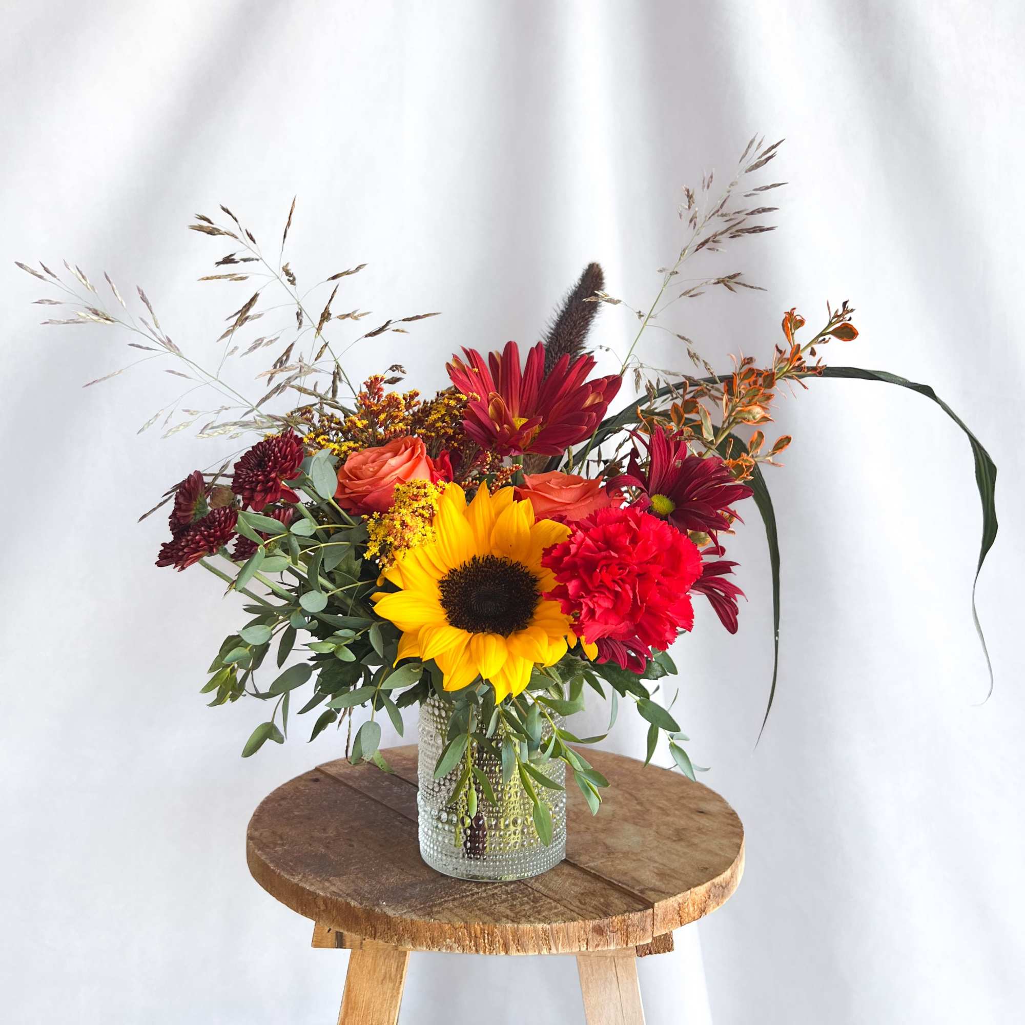 Mixed bouquet in a glass vase with sunflowers, roses, and red blooms