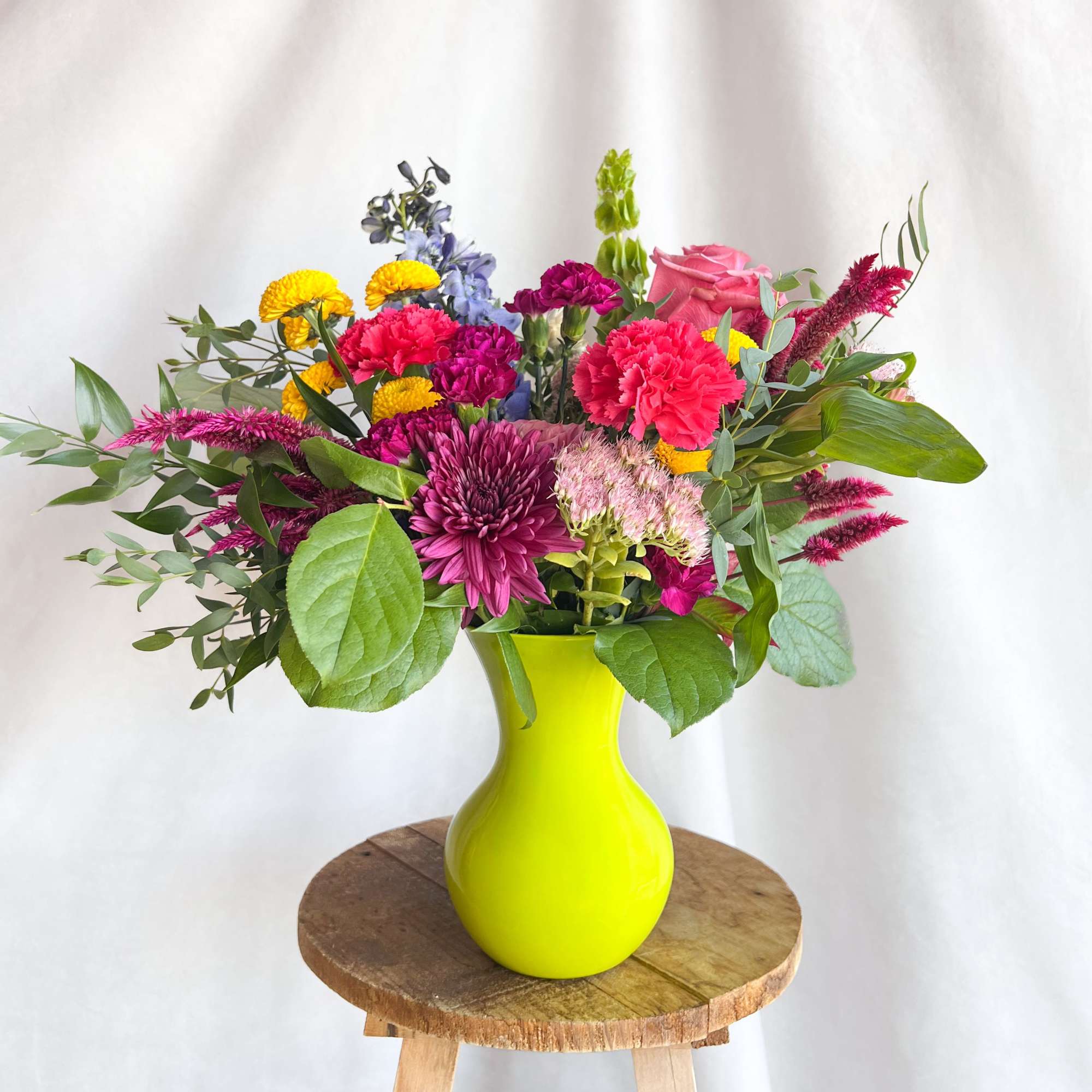 Mixed bouquet in a bright yellow vase with pink, purple, and yellow flowers