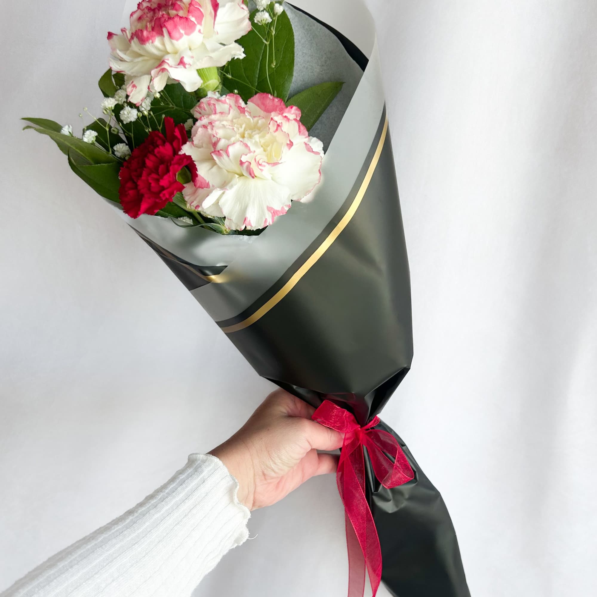 Handheld bouquet of pink and white carnations wrapped in dark paper