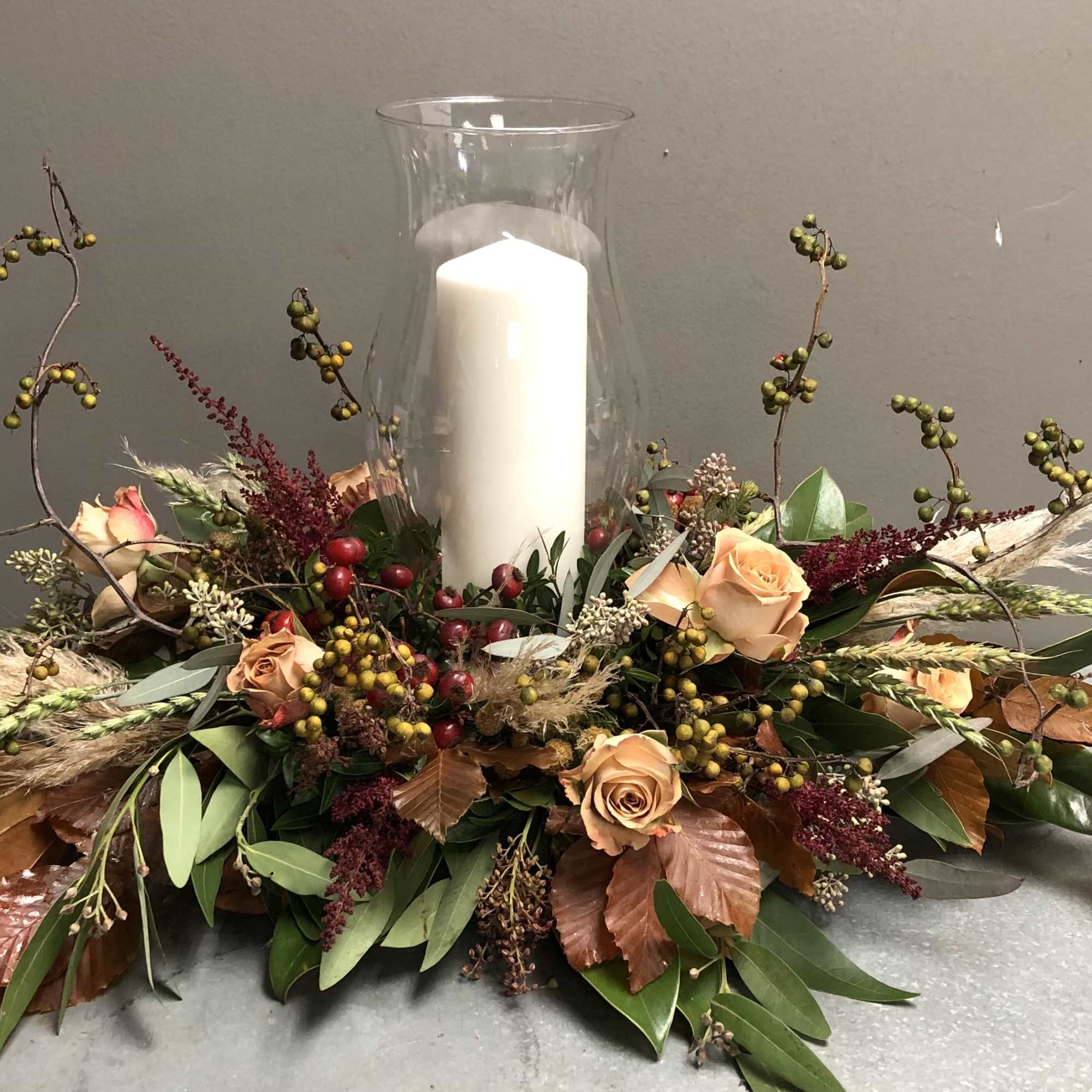 Low floral centerpiece with peach roses and a white pillar candle in a glass hurricane