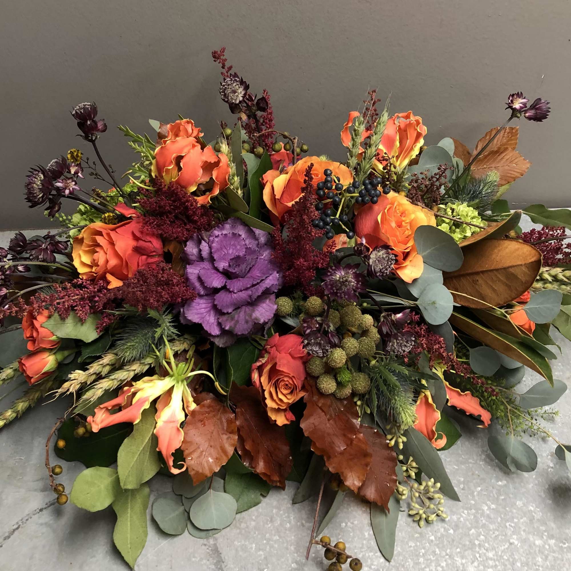 Low floral arrangement with orange roses, purple cabbage, and mixed foliage