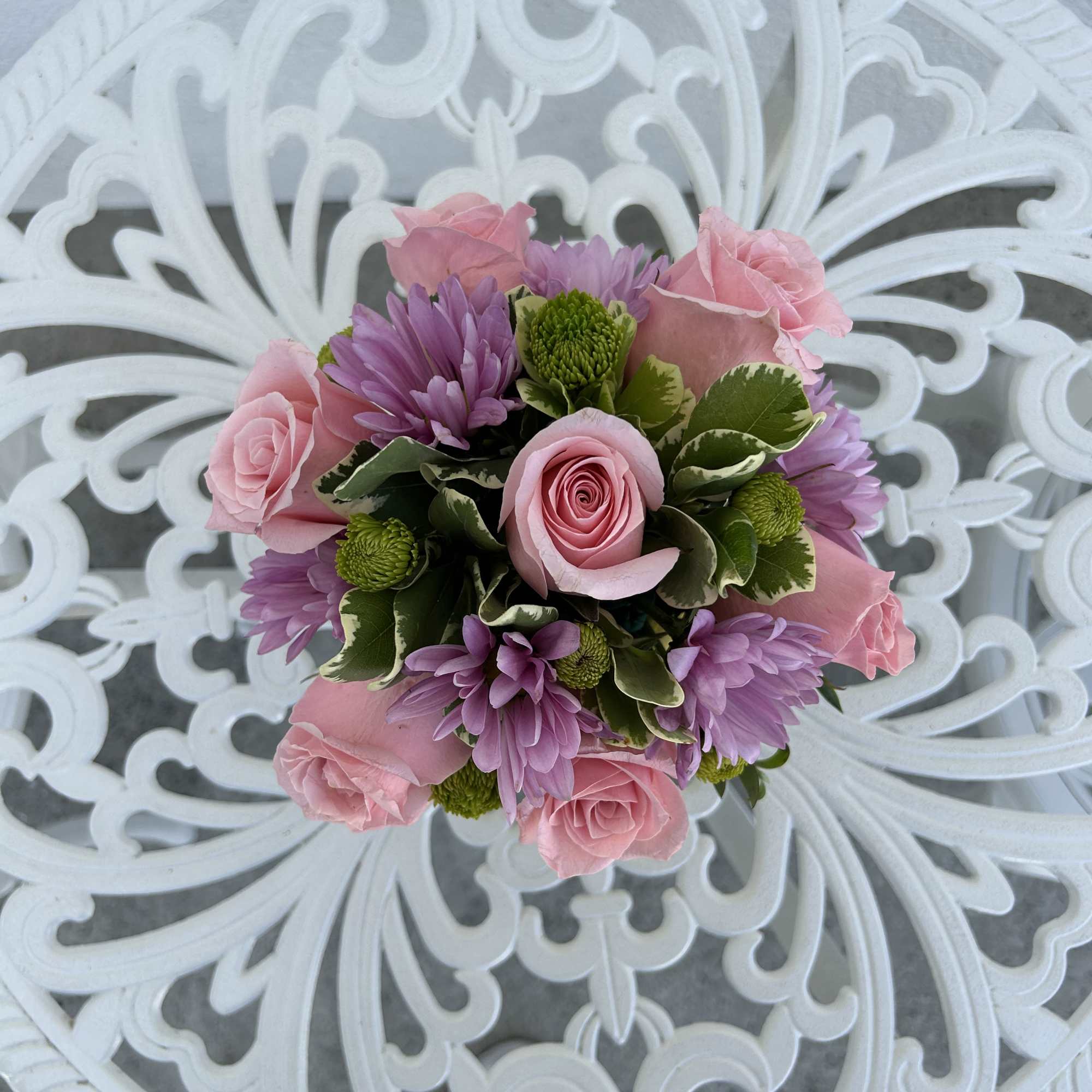 Pink roses and purple daisies arranged in a round bouquet