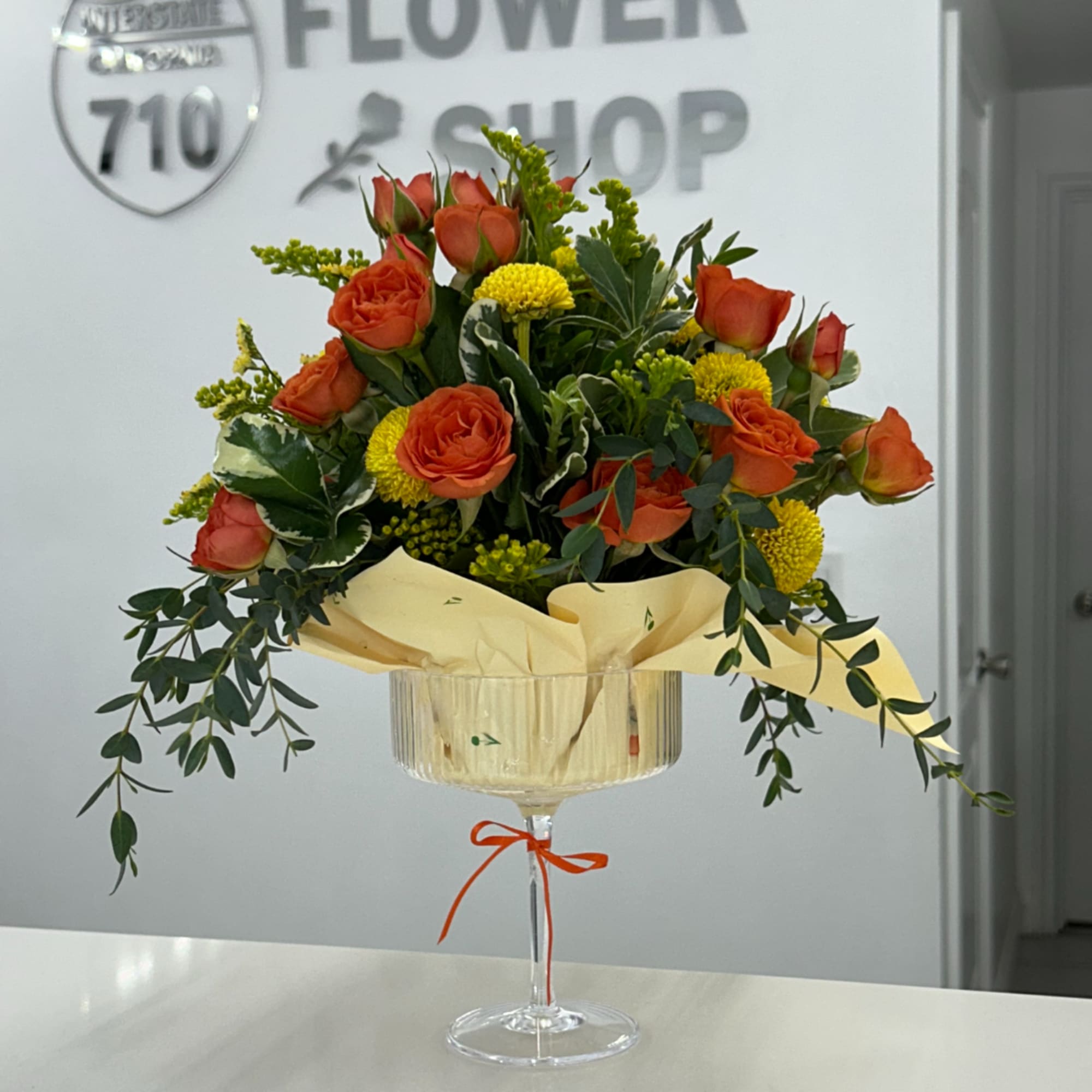 Orange roses and yellow mums in a stemmed glass vase with ribbon