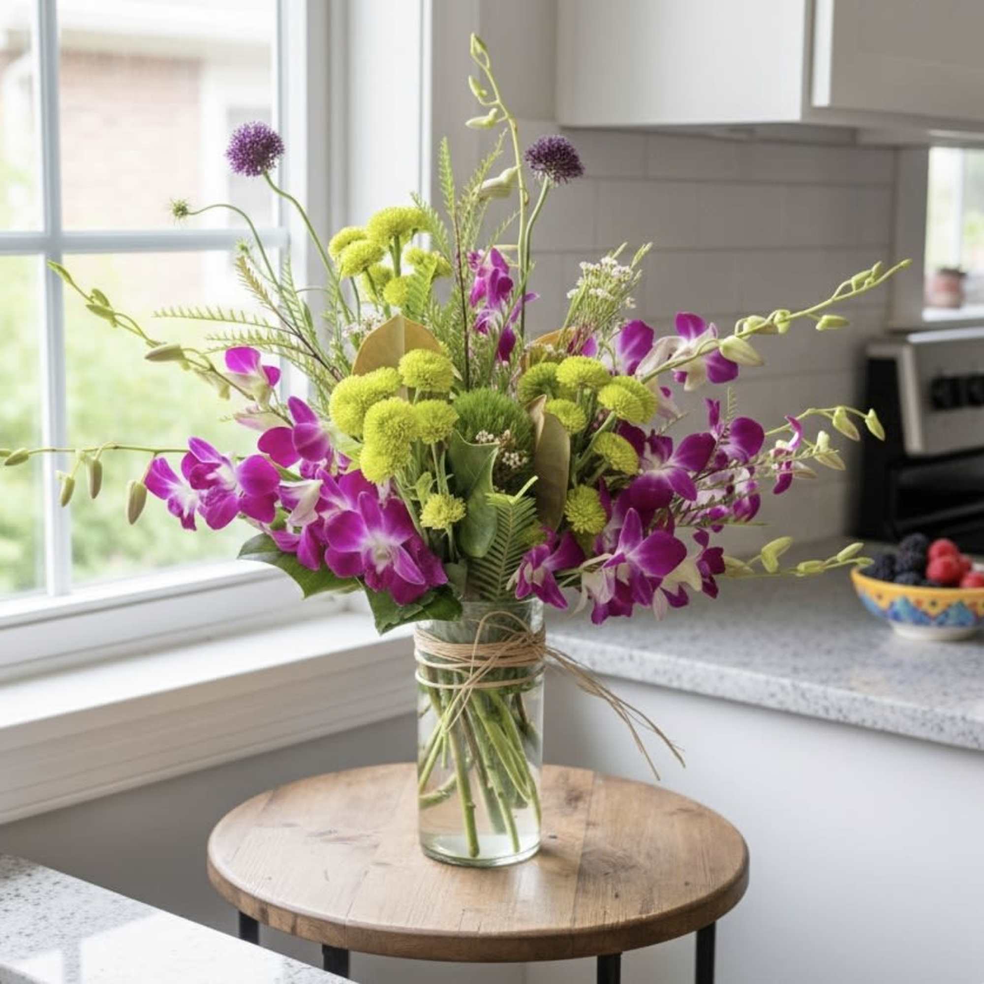 Purple orchids and green pom-pom flowers in a glass vase