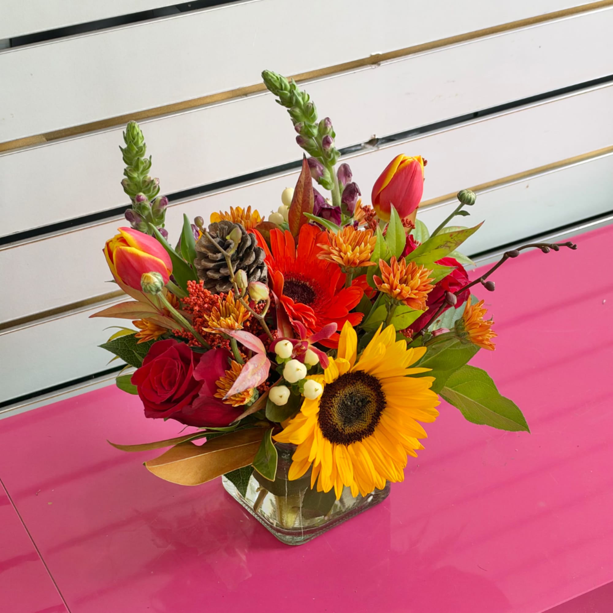 Colorful mixed bouquet in a square glass vase with sunflowers, roses, and tulips
