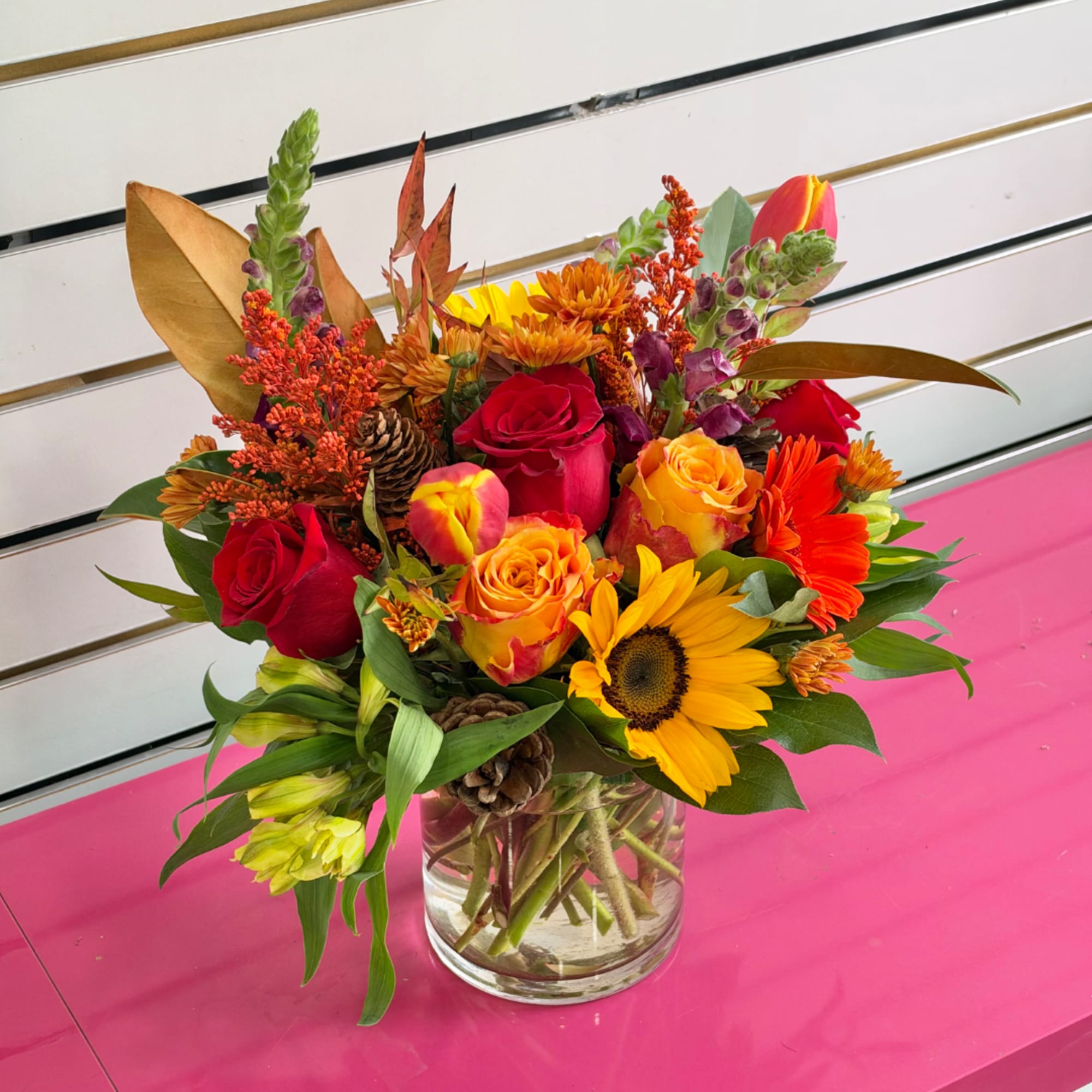 Mixed bouquet of roses, sunflowers, and orange blooms in a glass vase