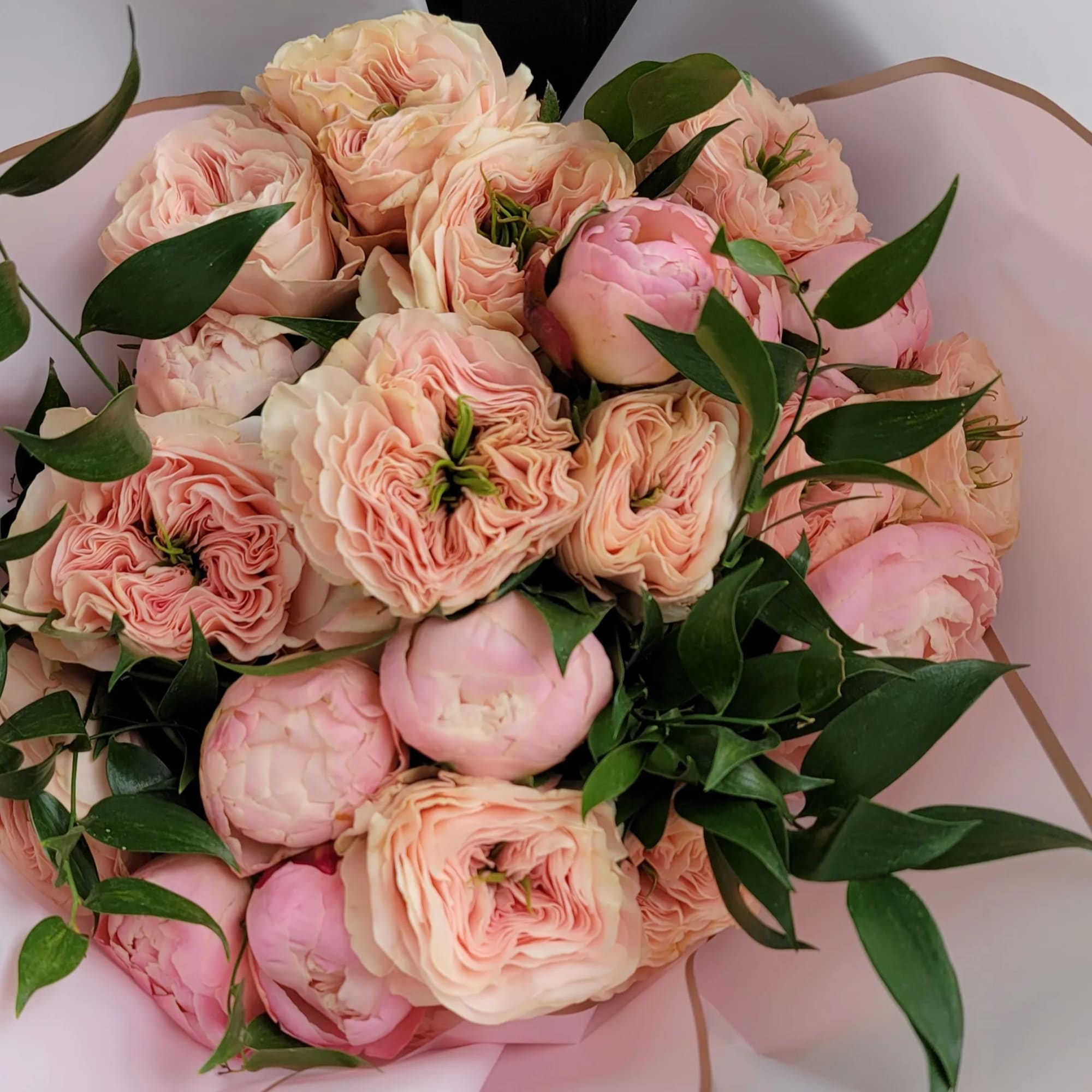 Bouquet of blush pink peonies and pale peach roses wrapped in pink paper