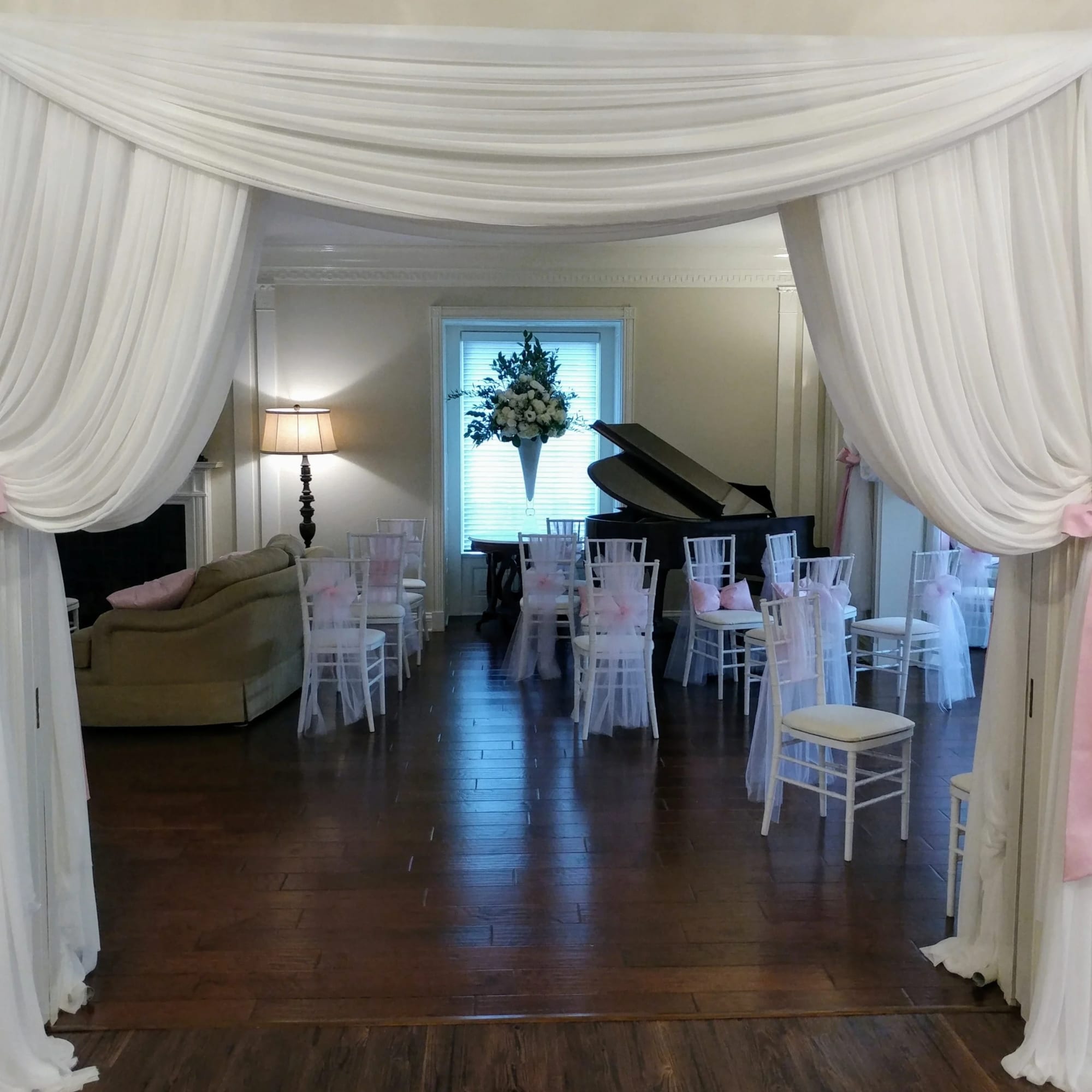 White draped archway with pink bows leading to a room with chairs and a floral arrangement