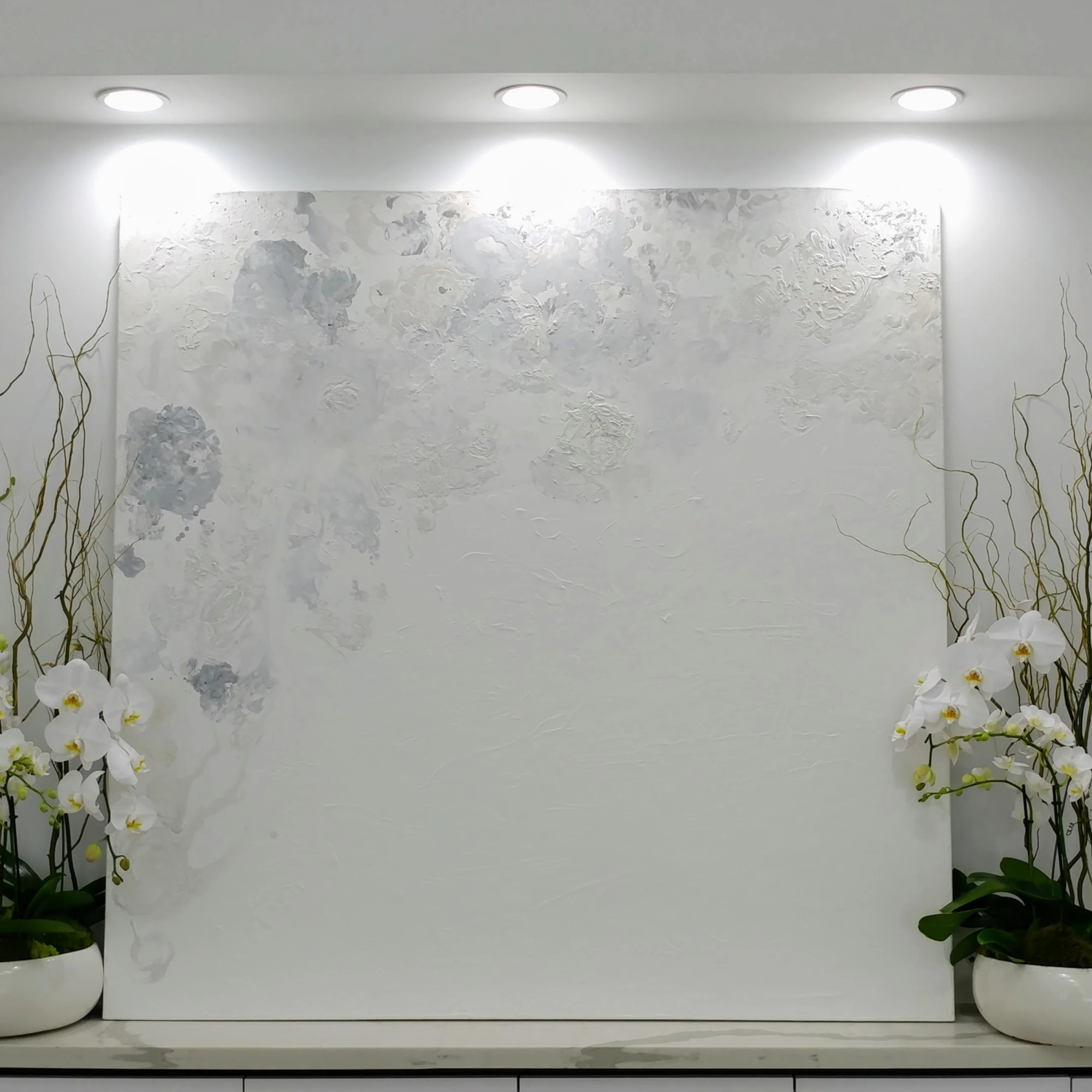 Two white orchid arrangements in low white bowls flank a large textured wall panel.