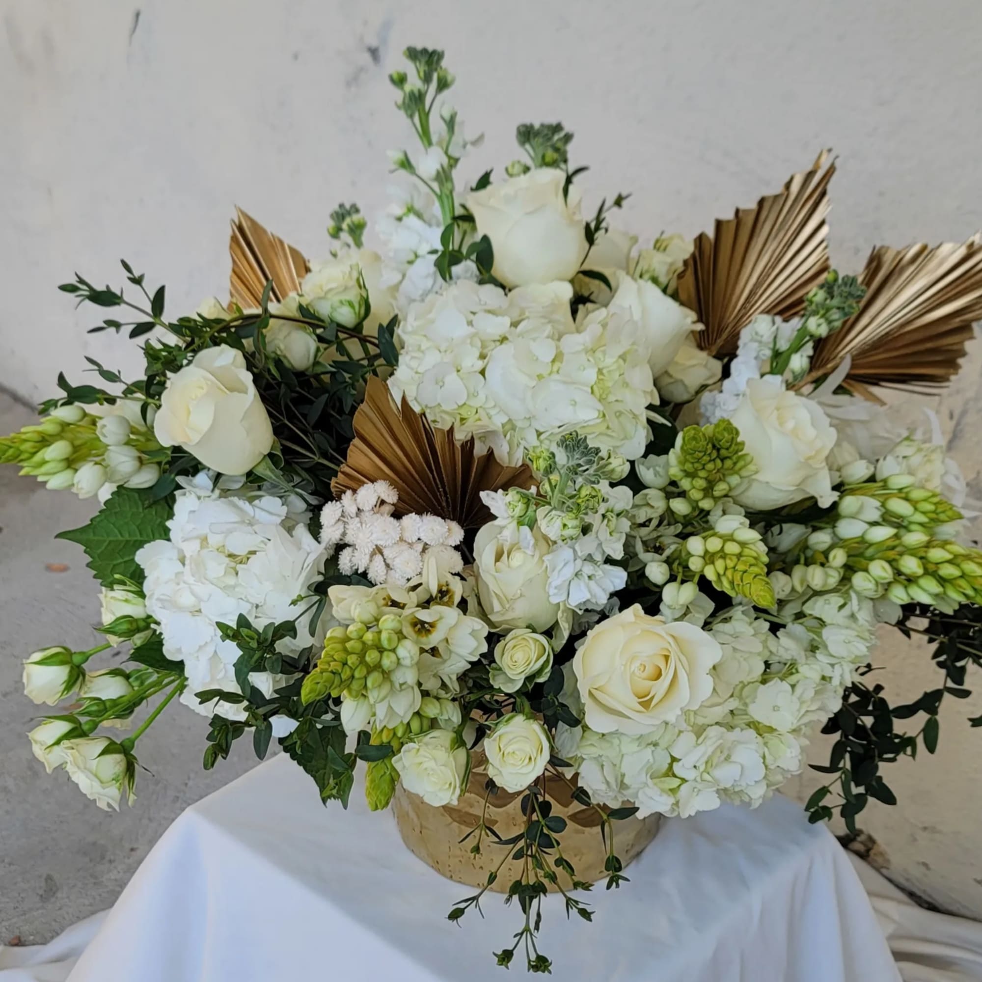 White floral arrangement with roses and hydrangeas in a gold container