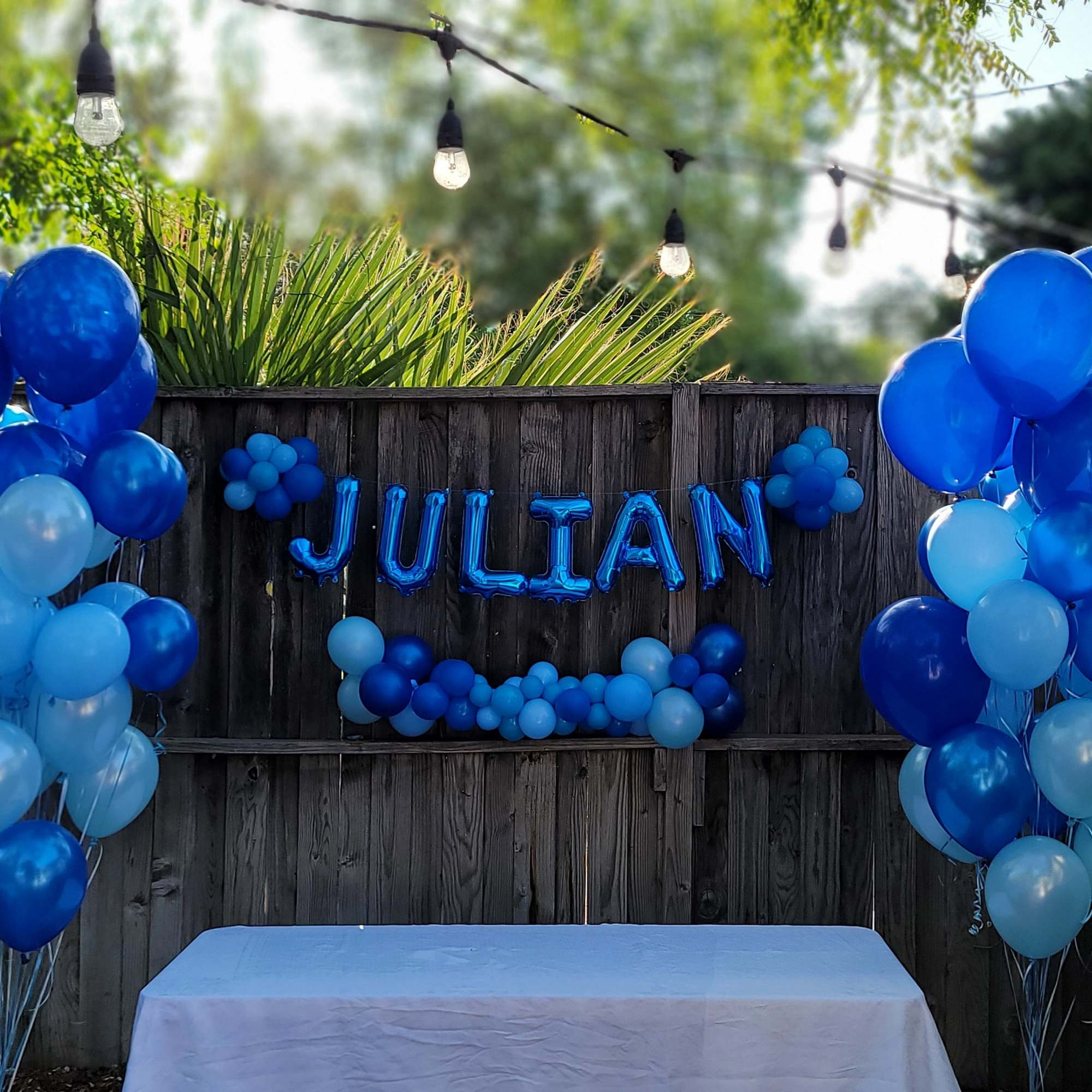 Blue balloon display with the name JULIAN on a backyard fence