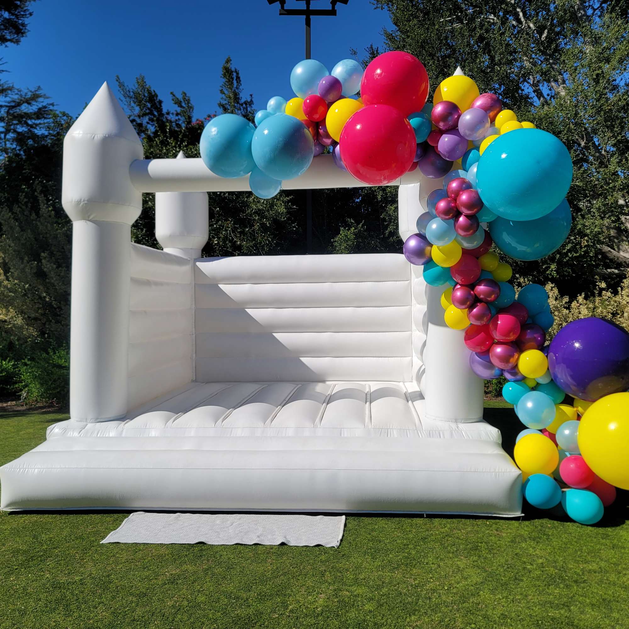 White inflatable bounce house decorated with colorful balloons outdoors.