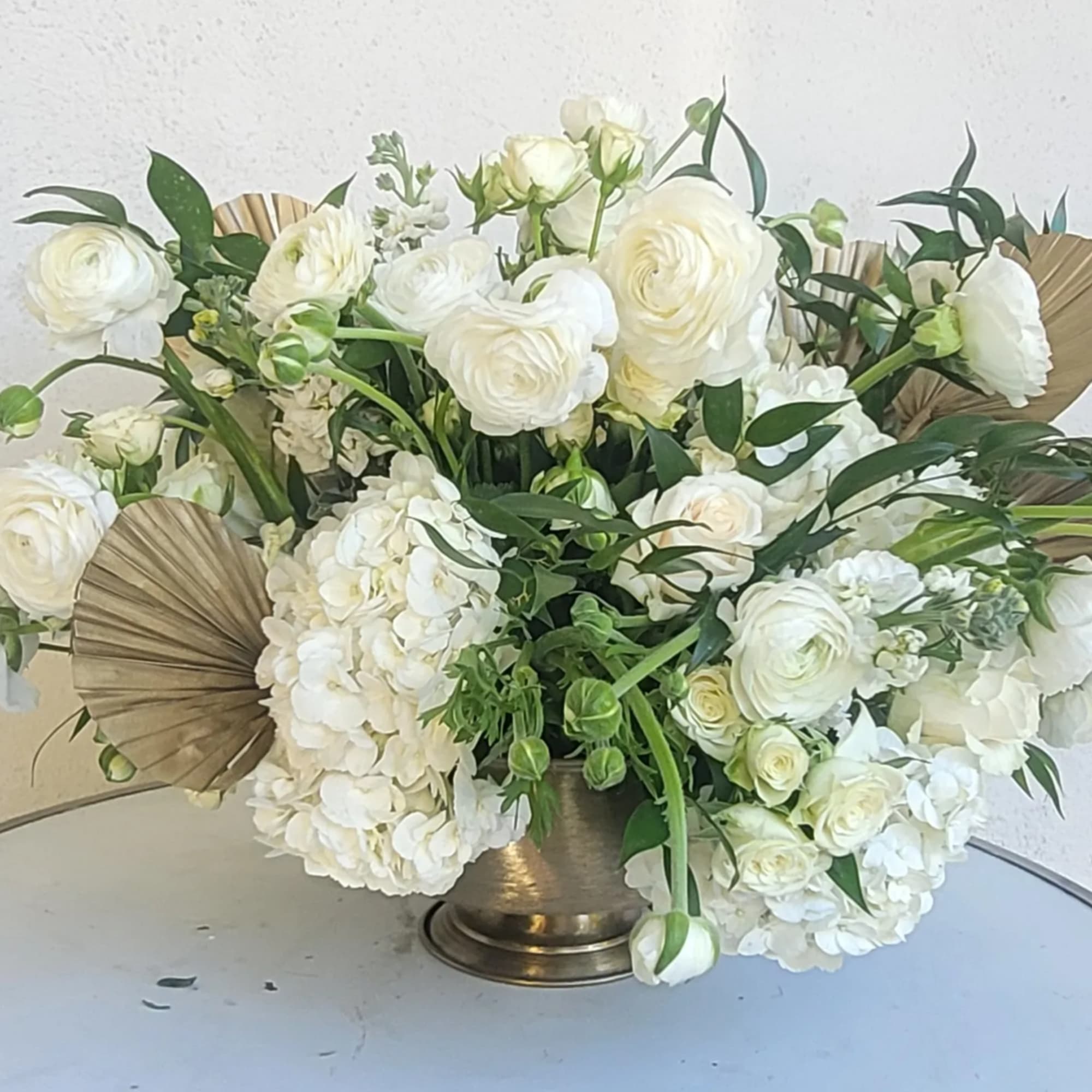 White floral arrangement in a bronze vase with fan accents
