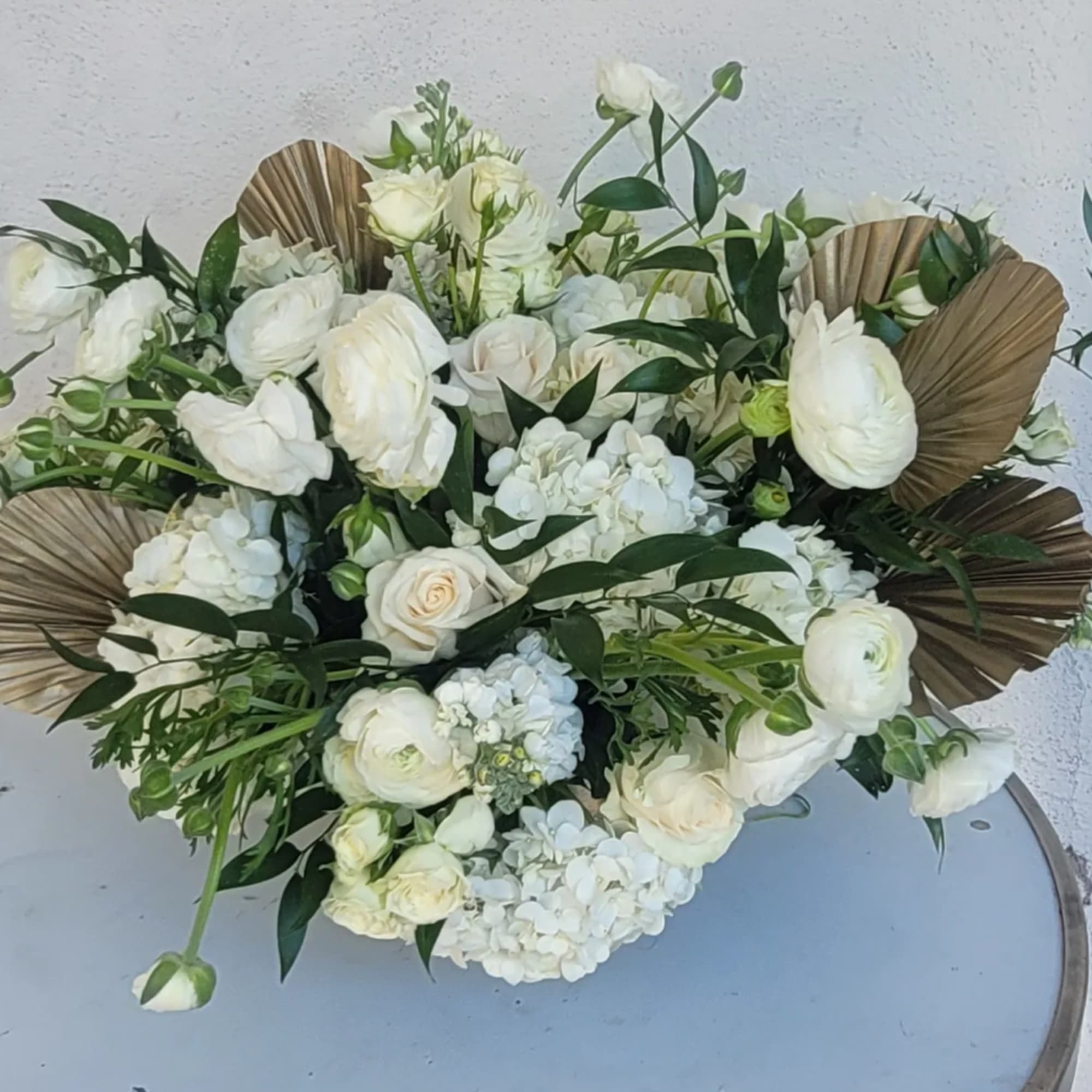 White floral arrangement with roses, ranunculus, and hydrangea in a low design