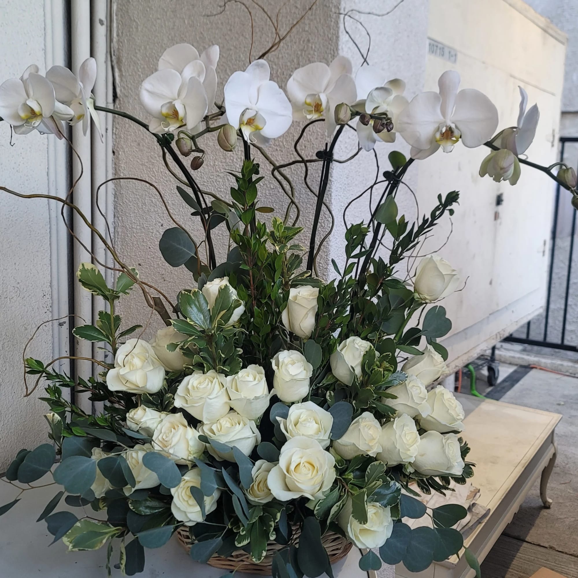White roses and orchids arranged in a basket with greenery