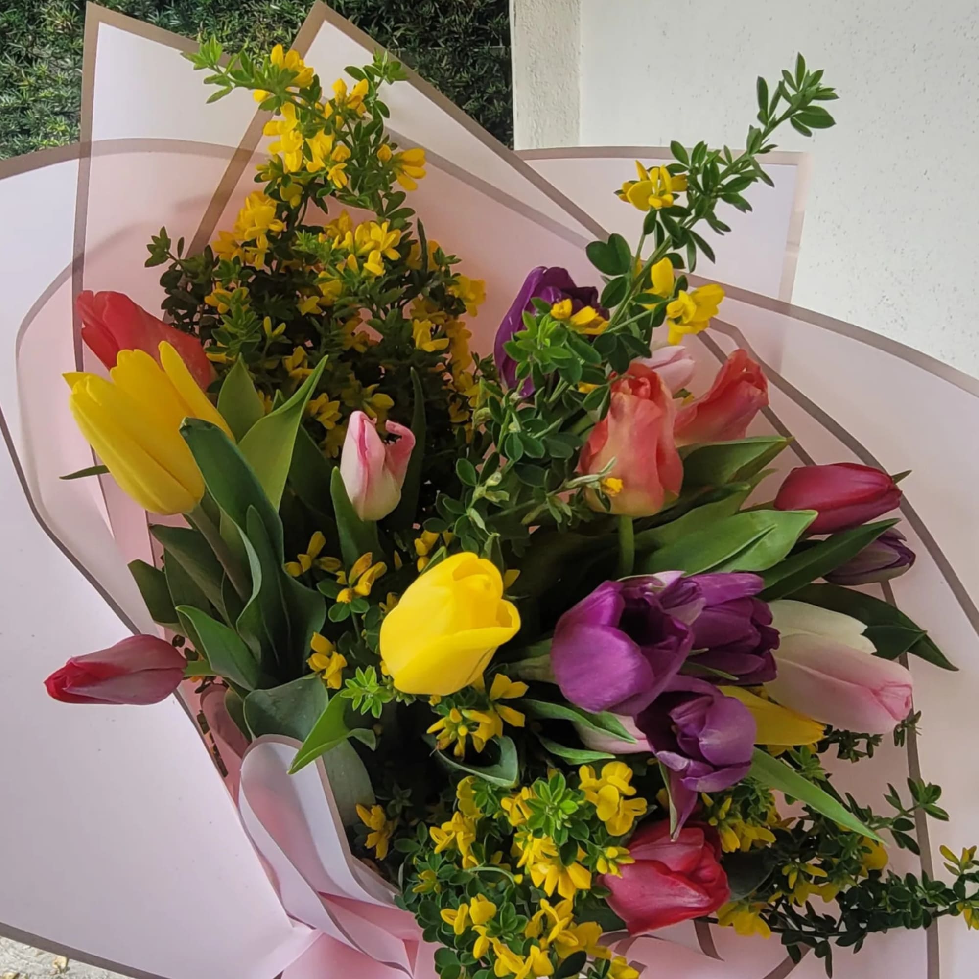 Bouquet of multicolored tulips with yellow filler flowers wrapped in pale pink paper