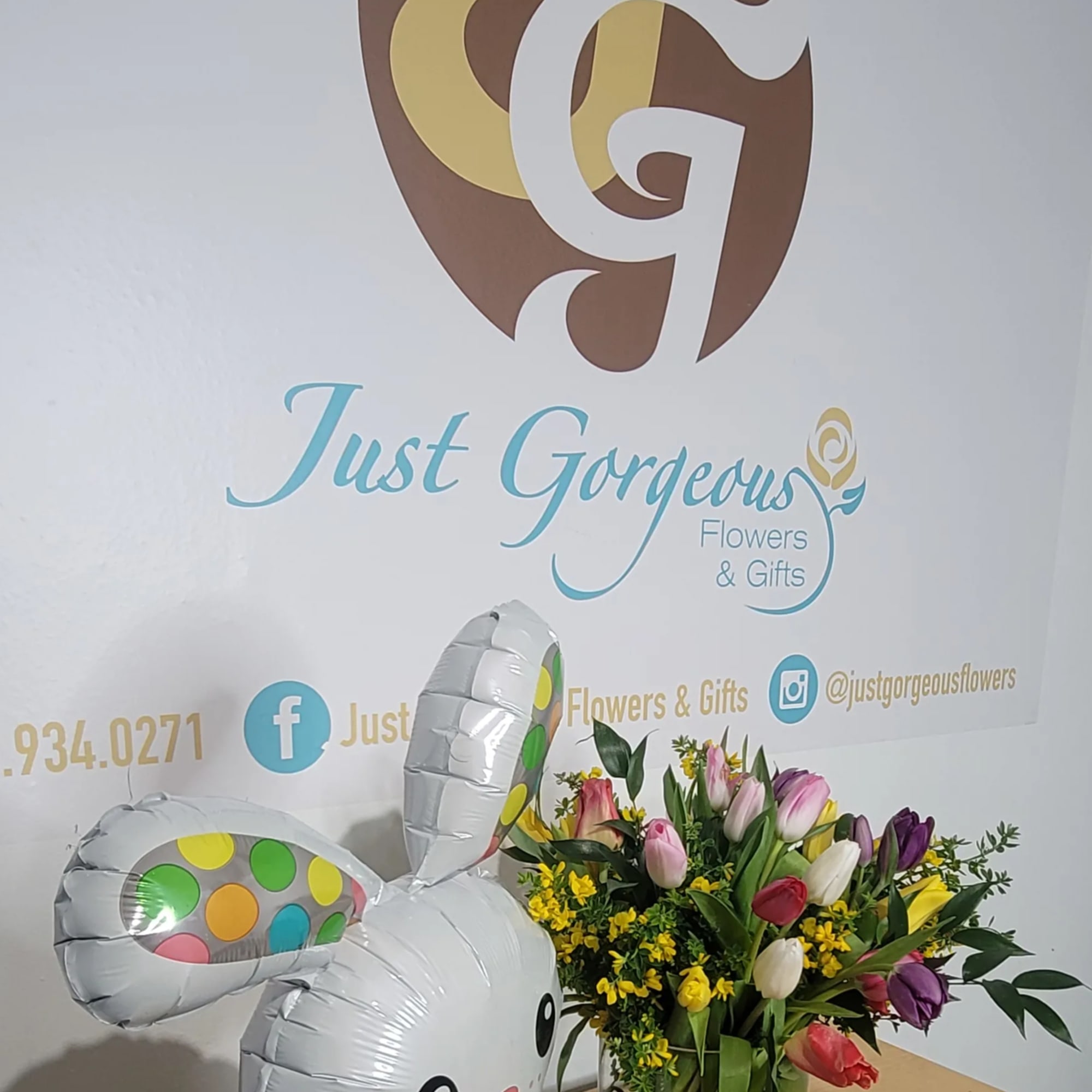 A bunny-shaped balloon beside a vase of mixed tulips and yellow flowers.