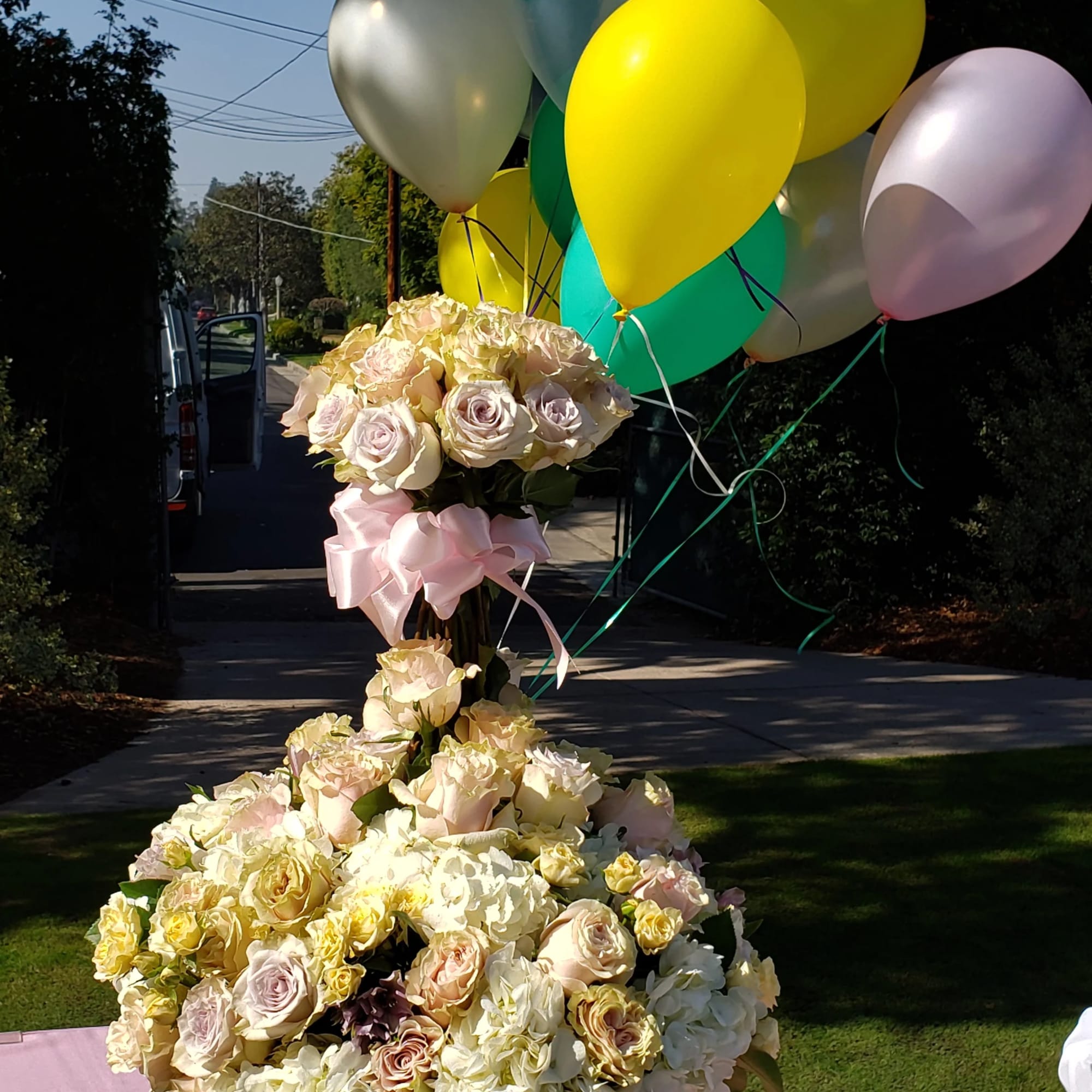 Cream rose arrangement in a white pedestal vase with pastel balloons
