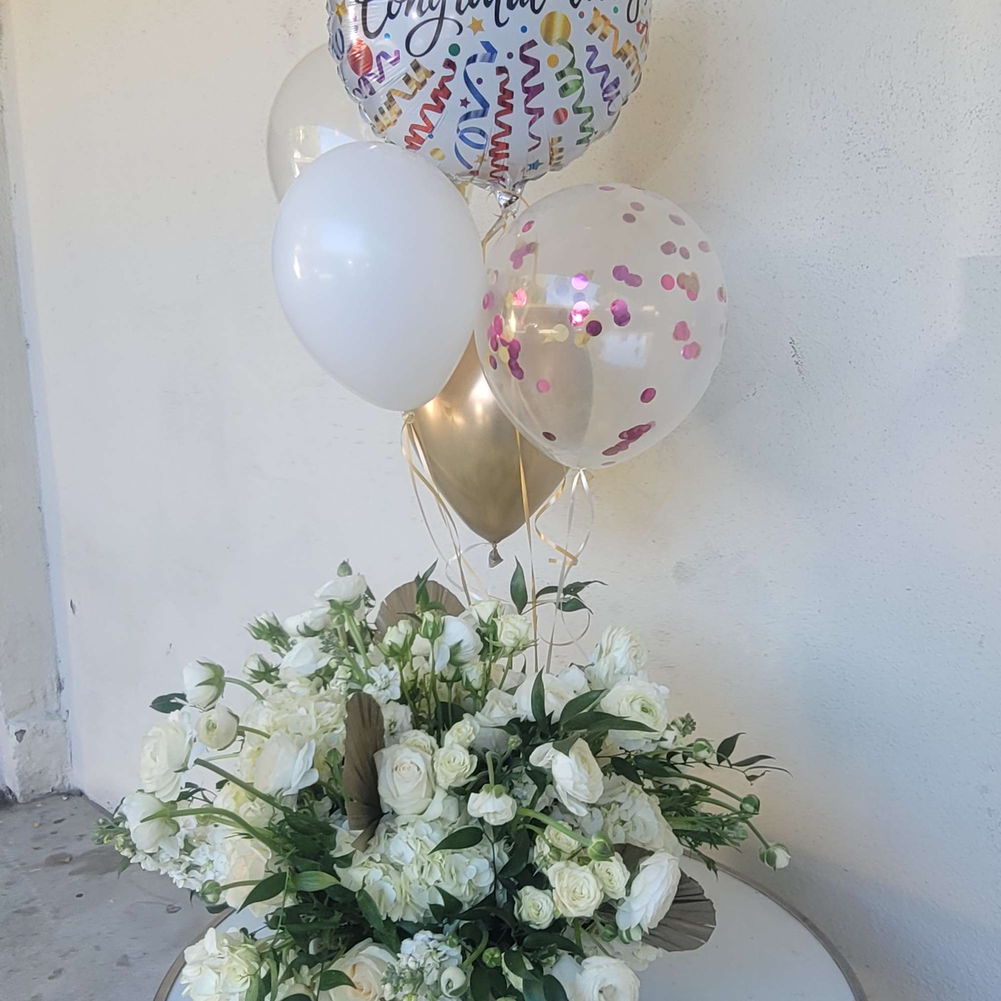 White floral arrangement with congratulatory balloons on a table