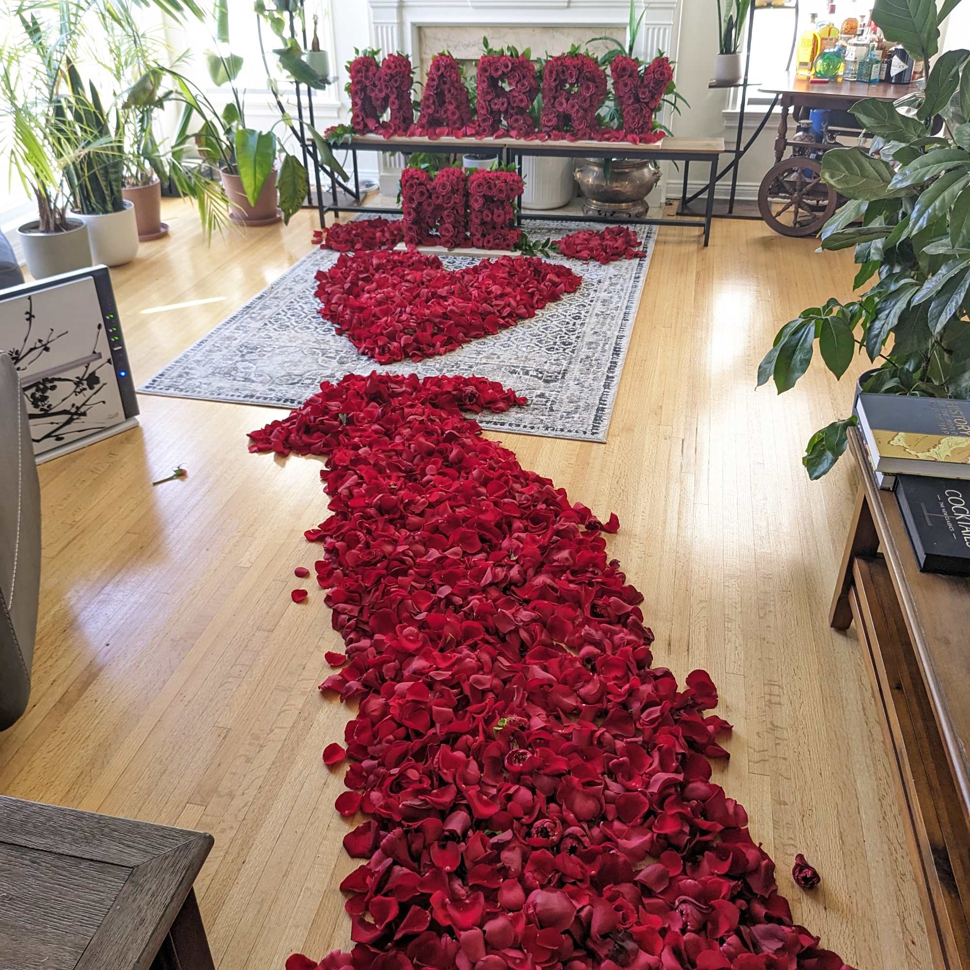 Red rose petals form a path leading to a floral "MARRY ME" display.
