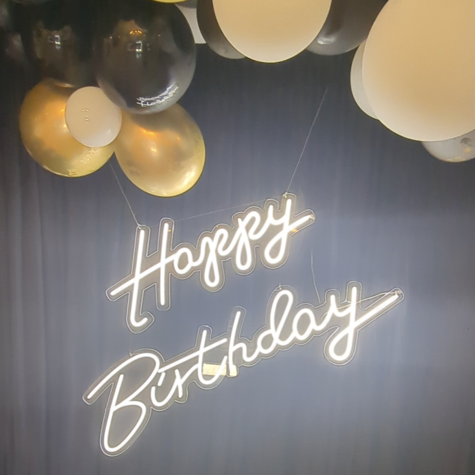 Birthday sign with gold, black, and white balloons overhead