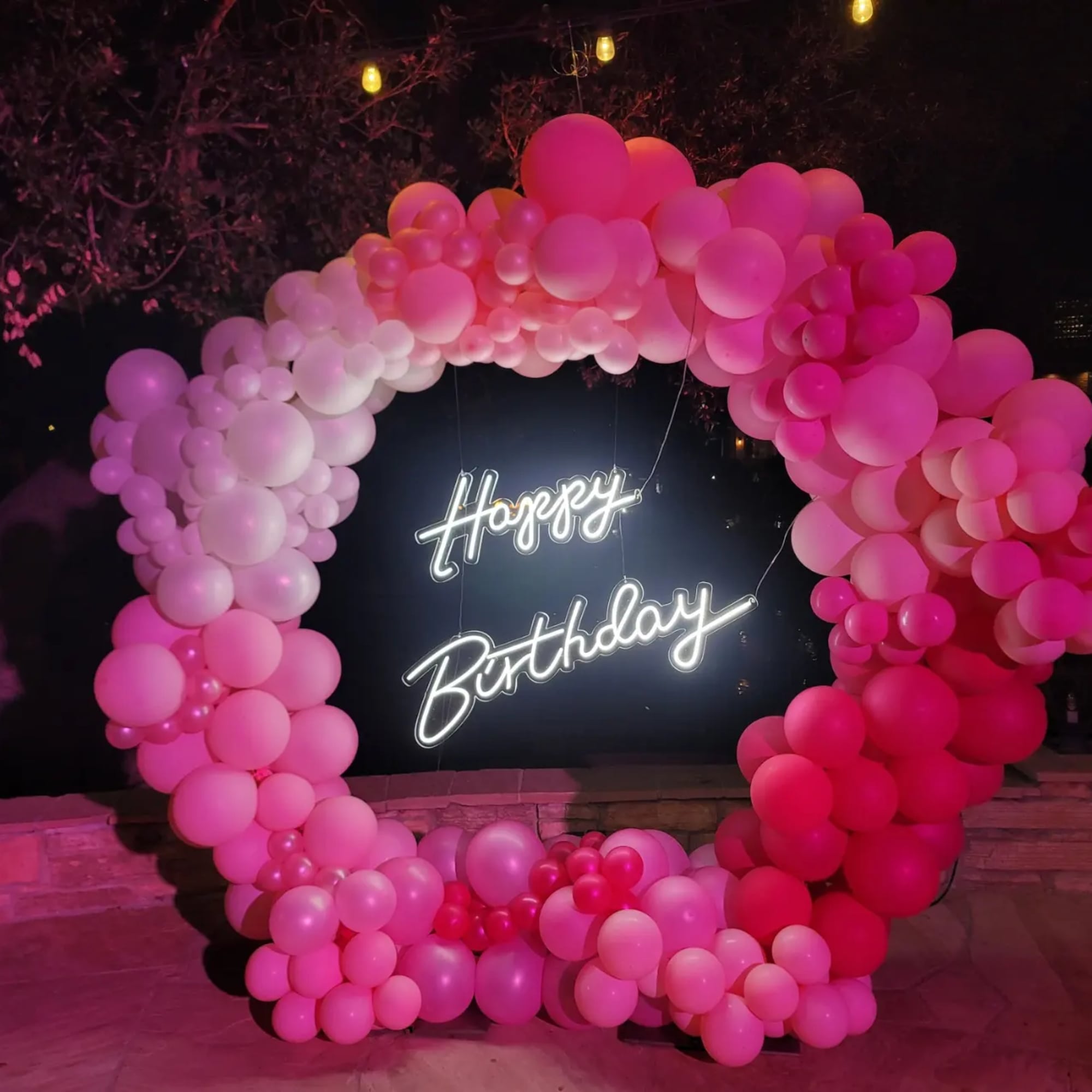 Pink balloon arch around a neon Happy Birthday sign