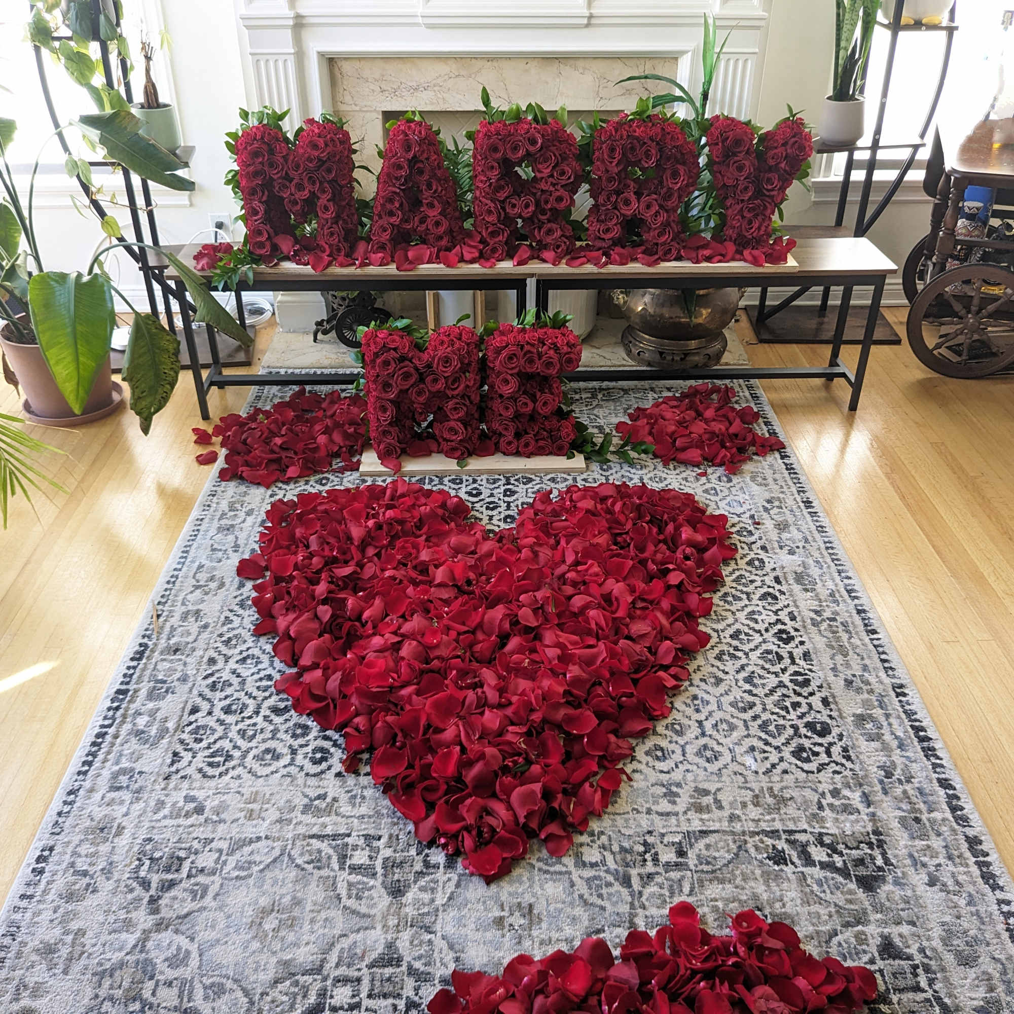 Red rose petals arranged in a heart shape with rose letter blocks on a table