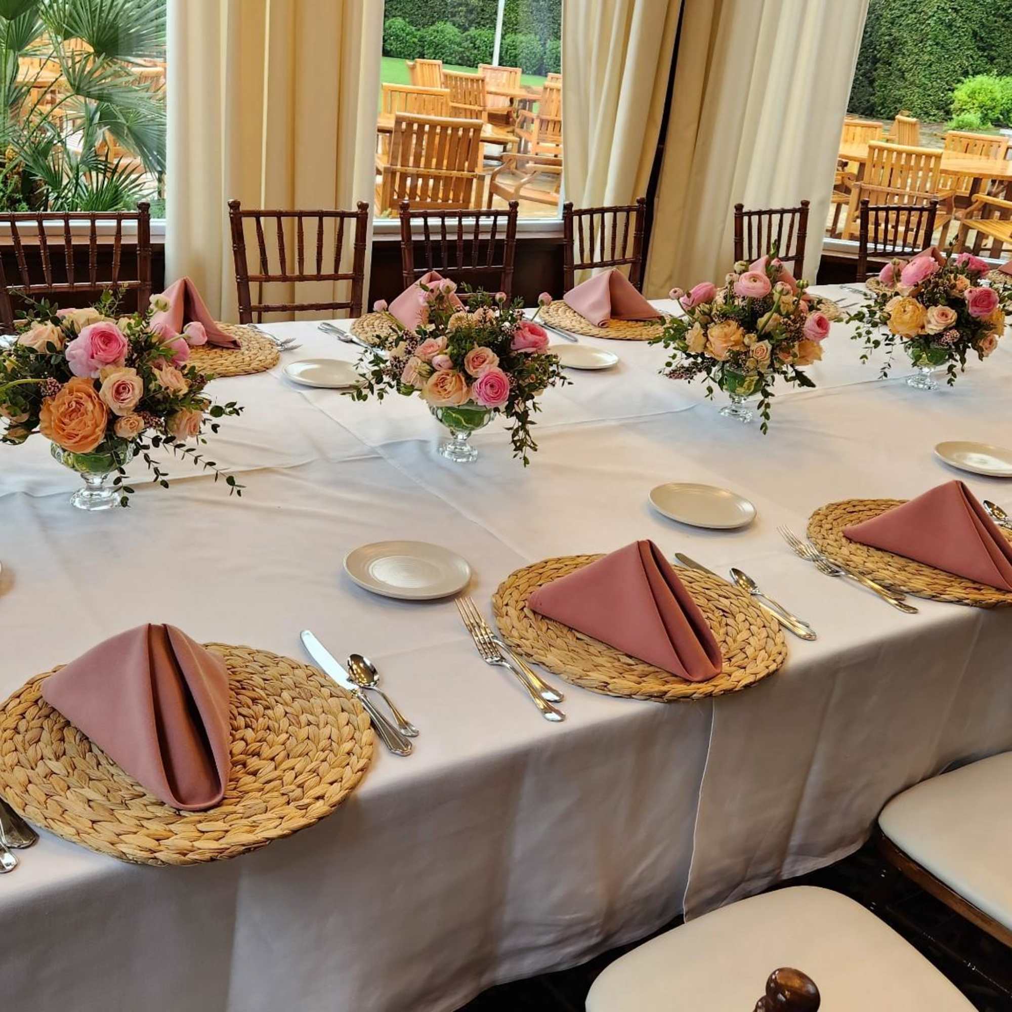 Floral centerpieces on a set dining table with pink napkins and woven placemats
