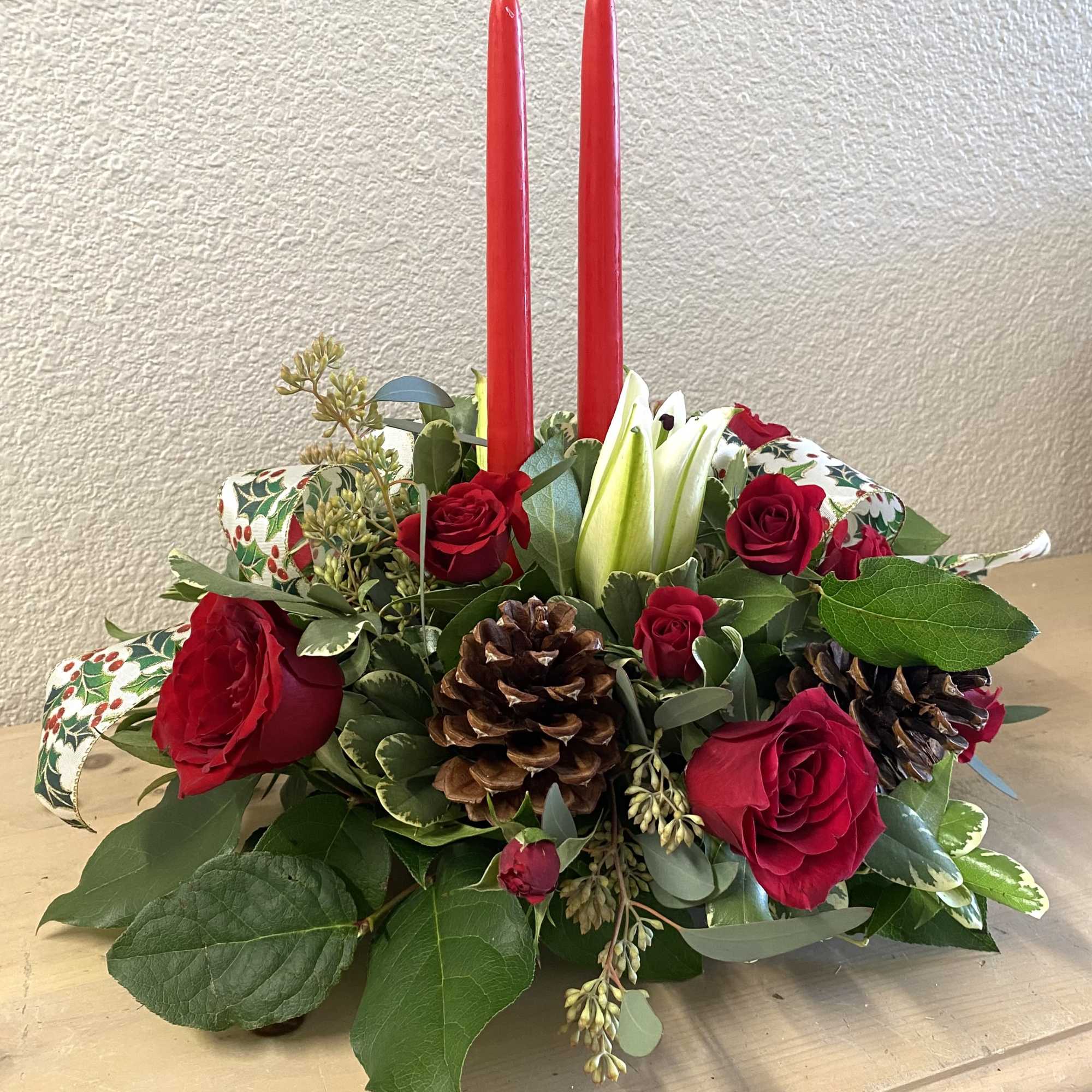 Red roses and candles arranged with pinecones in a low centerpiece.