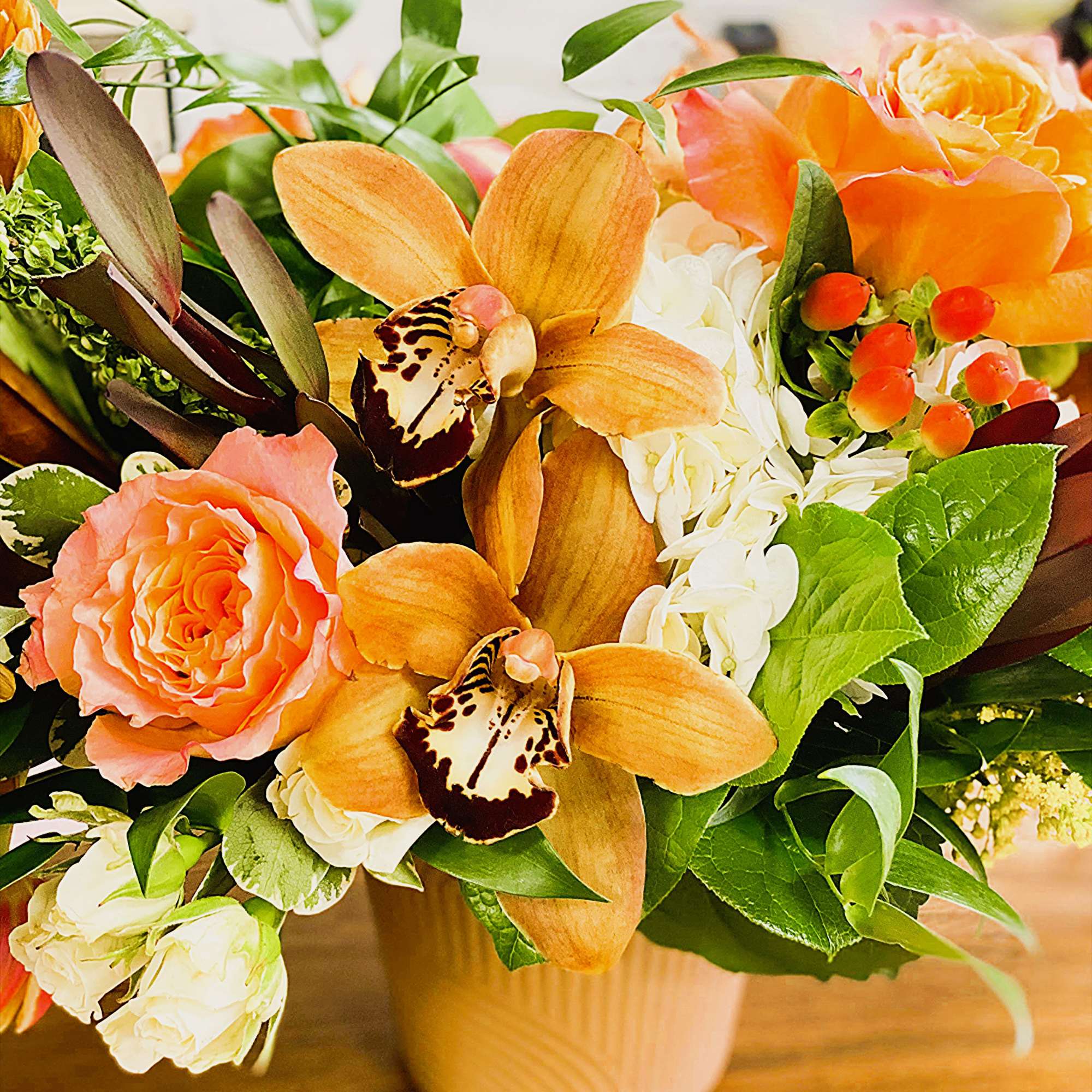 Orange roses and orchids arranged in a beige vase