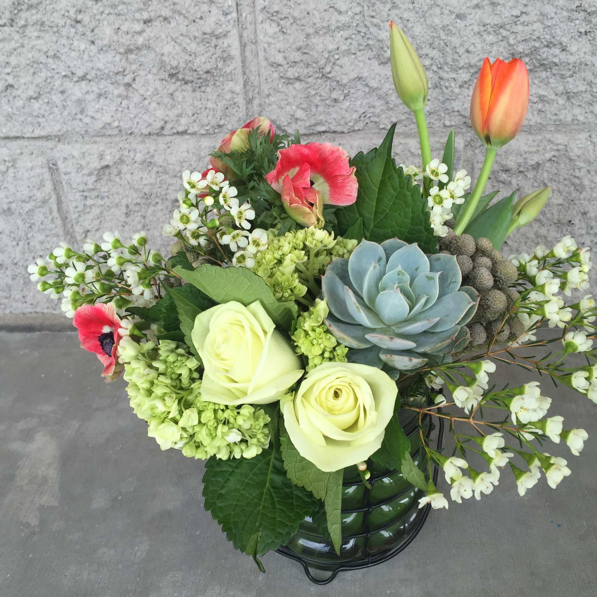 Mixed bouquet with pale roses, tulips, and a blue succulent in a glass vase