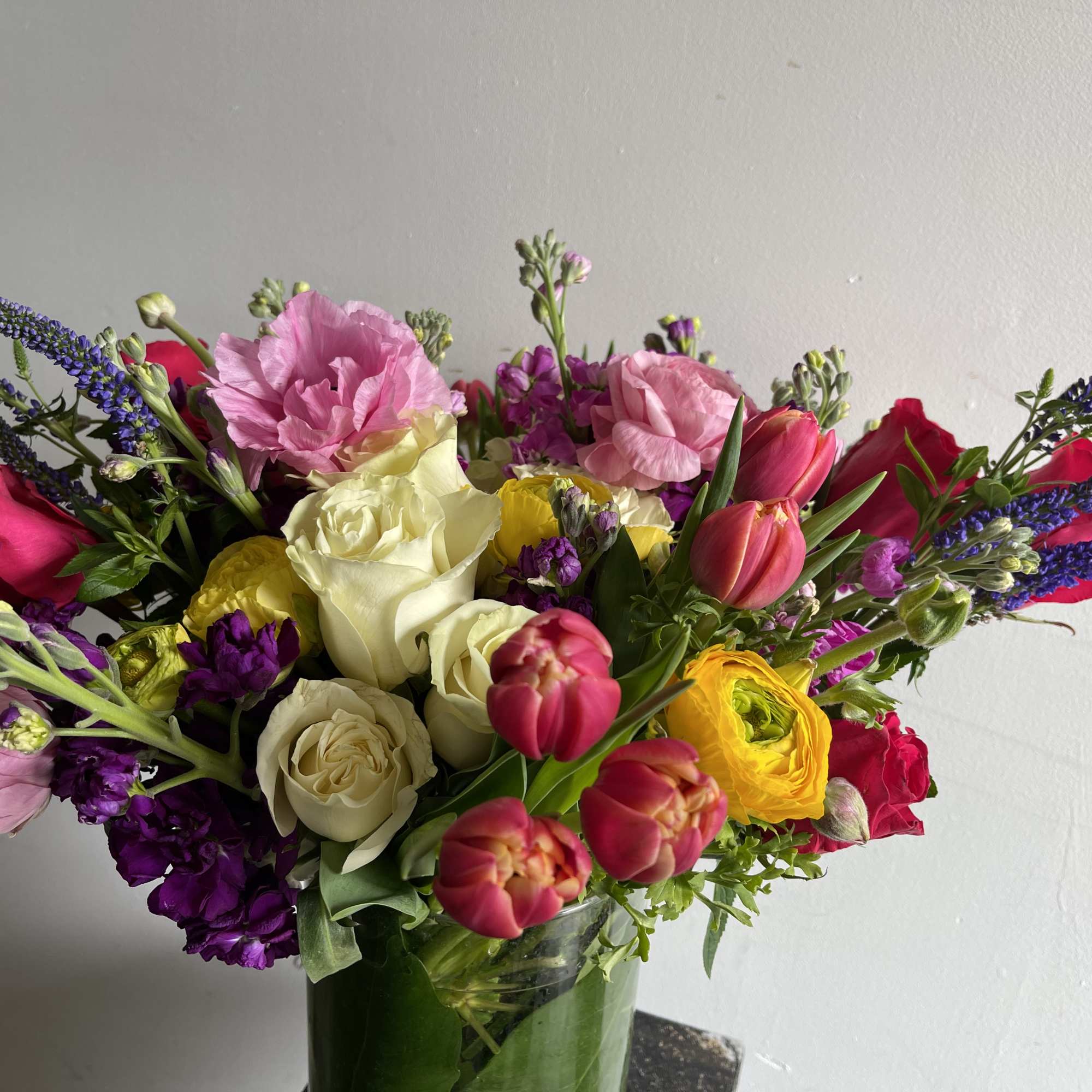 Mixed bouquet of roses, tulips, and purple spikes in a glass vase