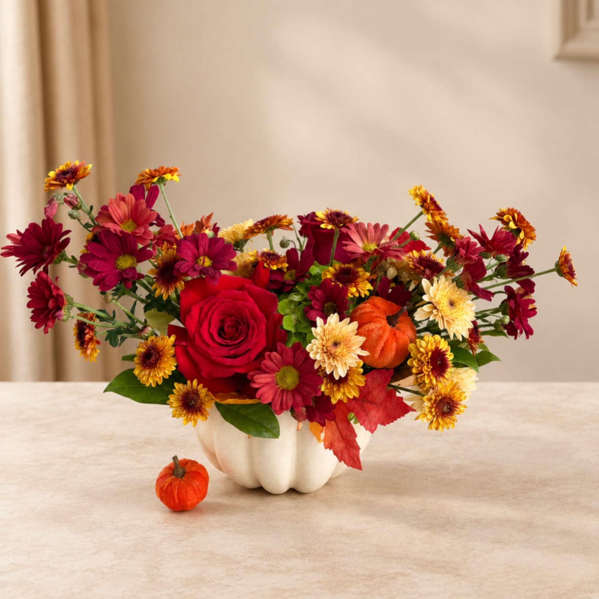 Fall floral arrangement in a white pumpkin vase with a small pumpkin on the table
